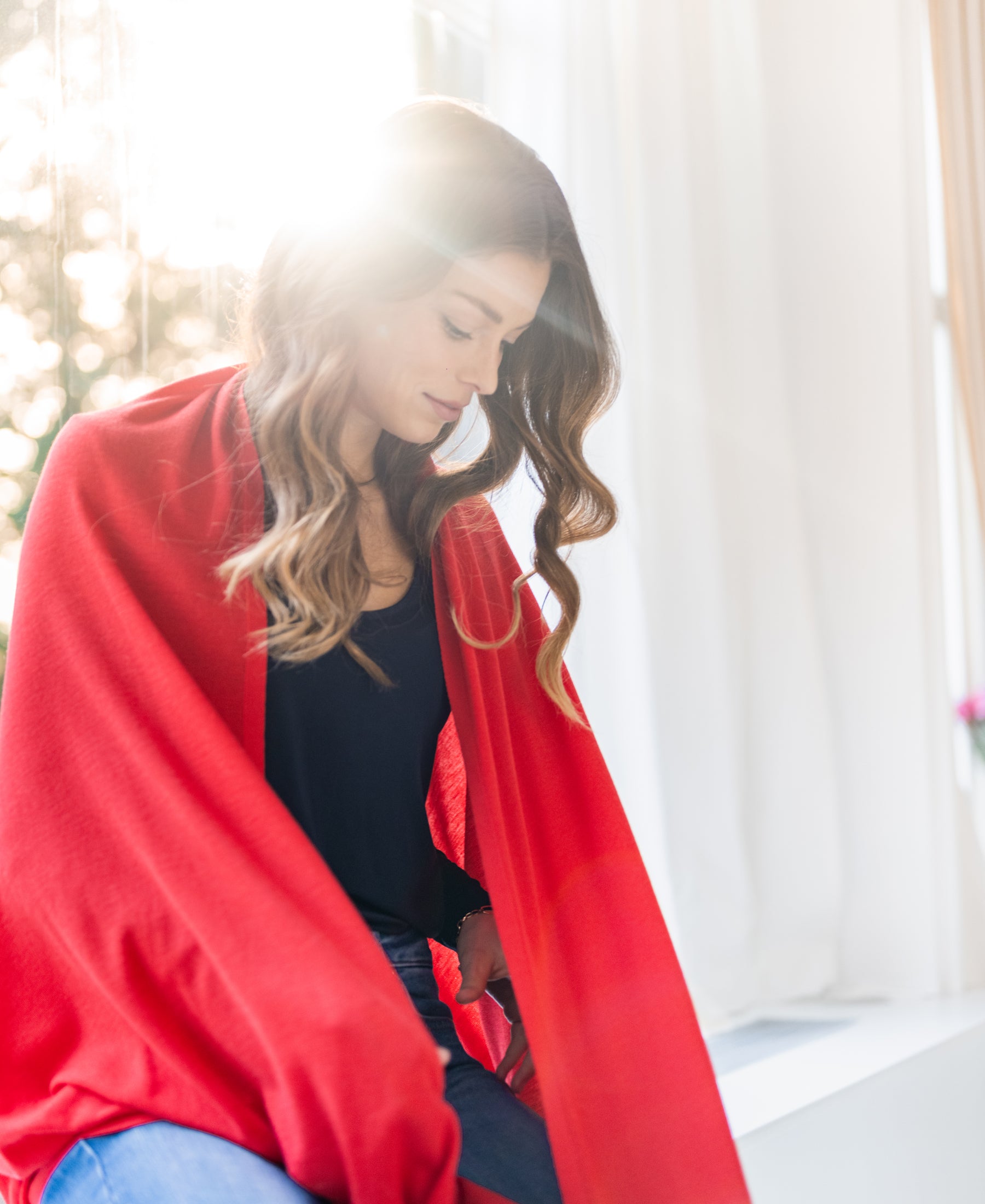 Coral red merino wool wrap LA BELLA by PLEIN PUBLIQUE shown by a sunlit window.