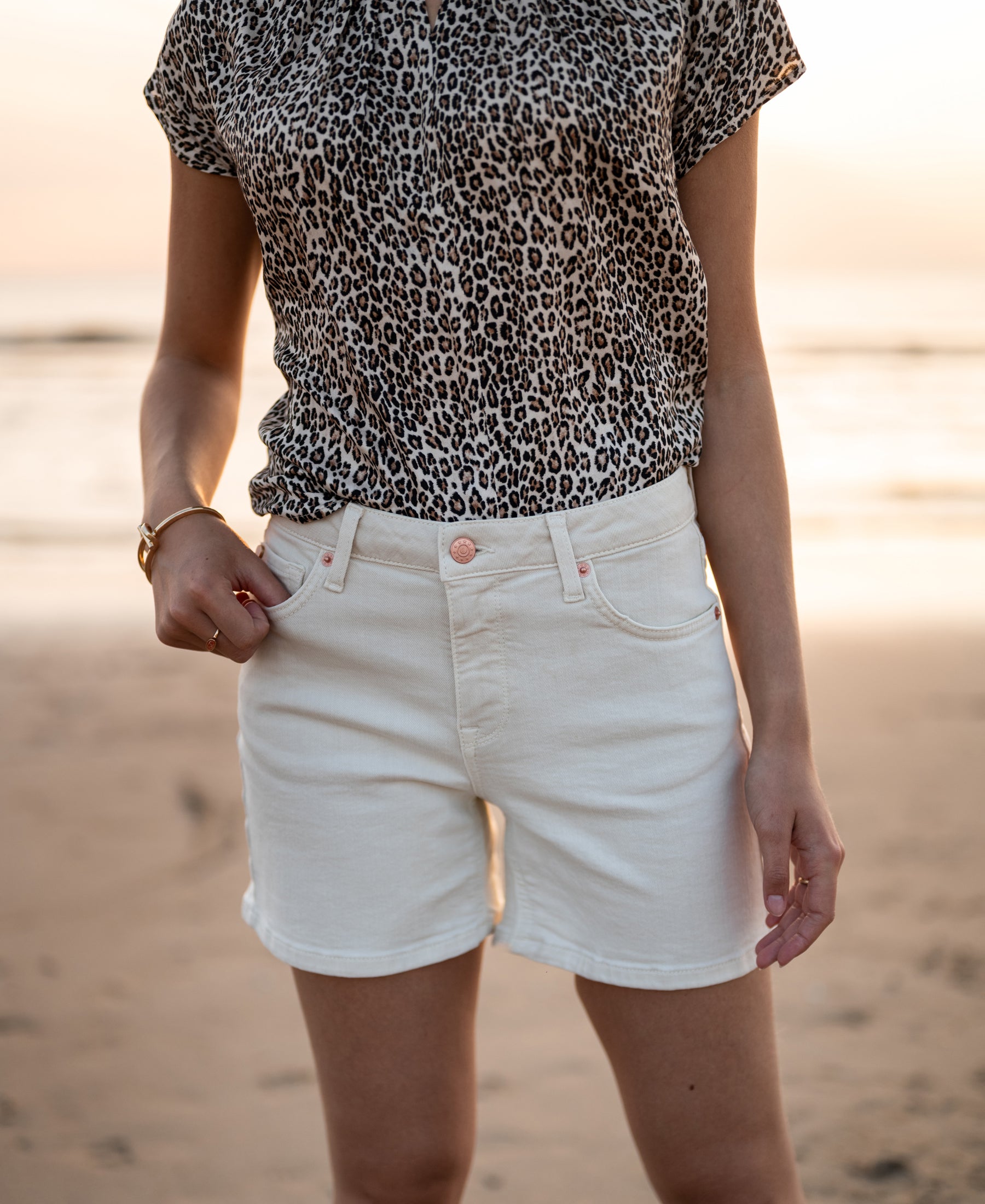 Cream-colored LA BILLY short by Plein Publique displayed on a person standing on a beach at sunset.