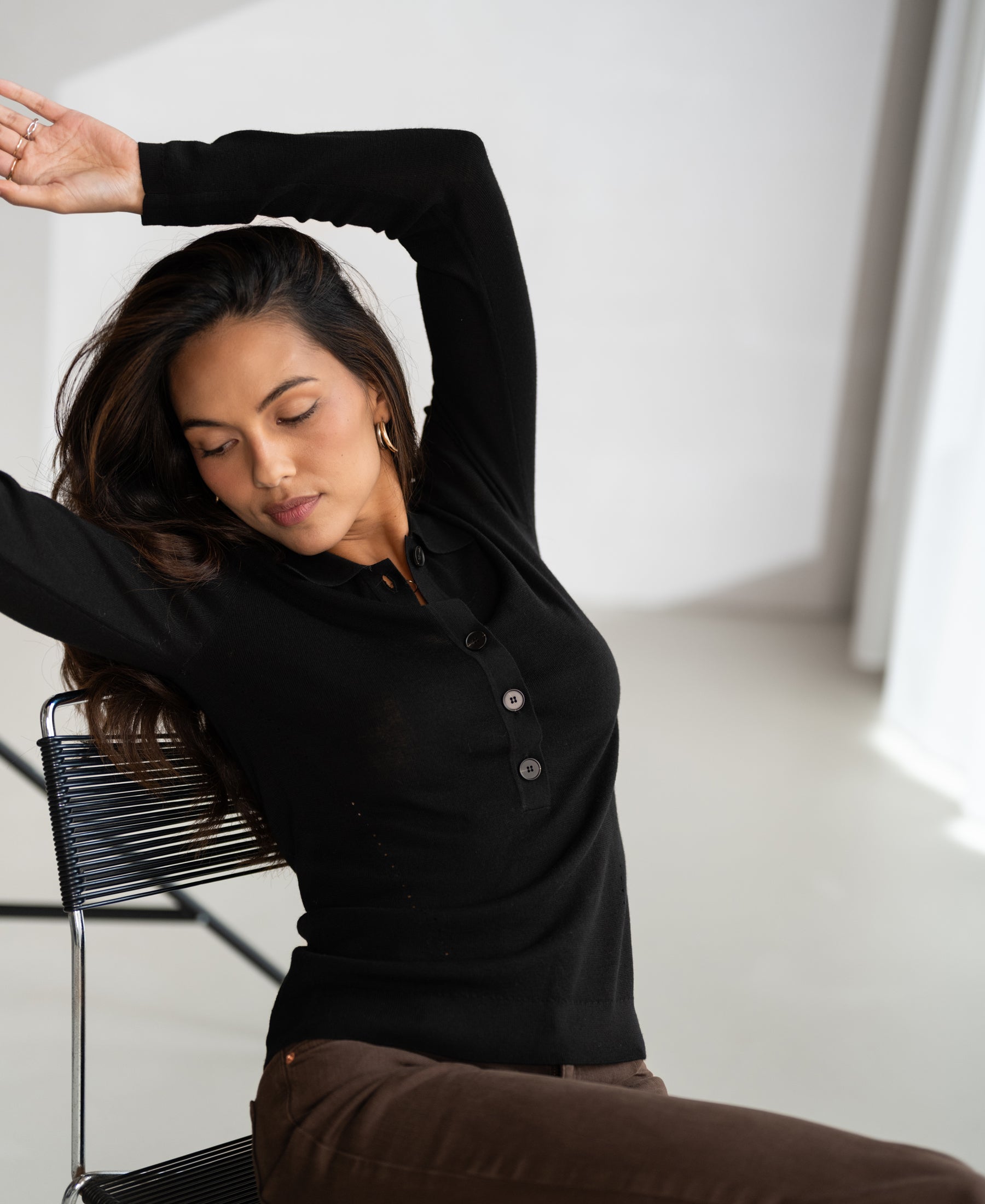 Black merino wool polo shirt by PLEIN PUBLIQUE, front view worn by a model sitting on a chair.