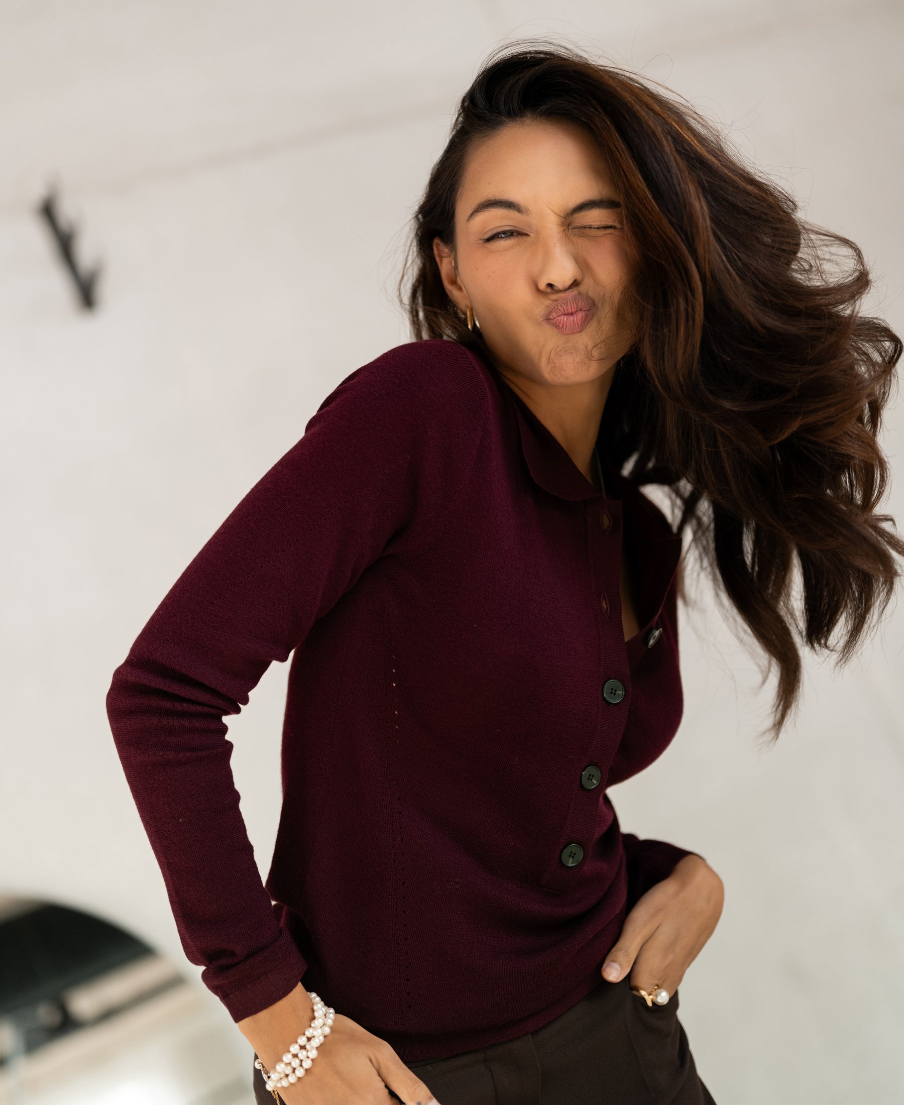 Bordeaux merino wool polo shirt, front view. Model winks and puckers her lips.