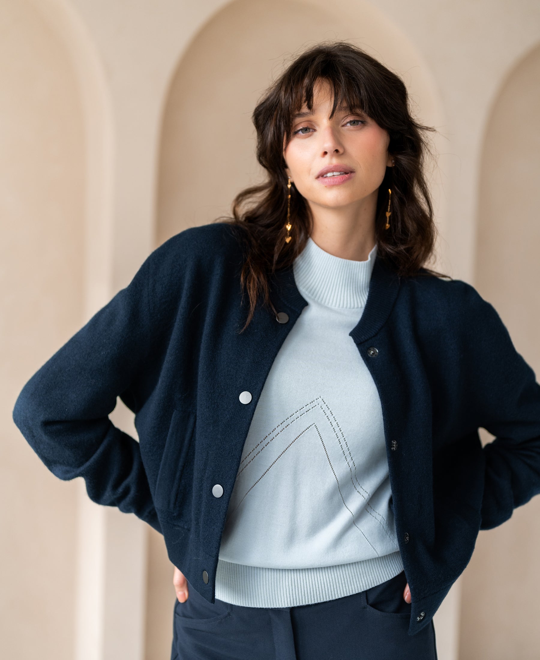 Front view of a dark blue bomber jacket with a wavy-haired model standing before an arched background.