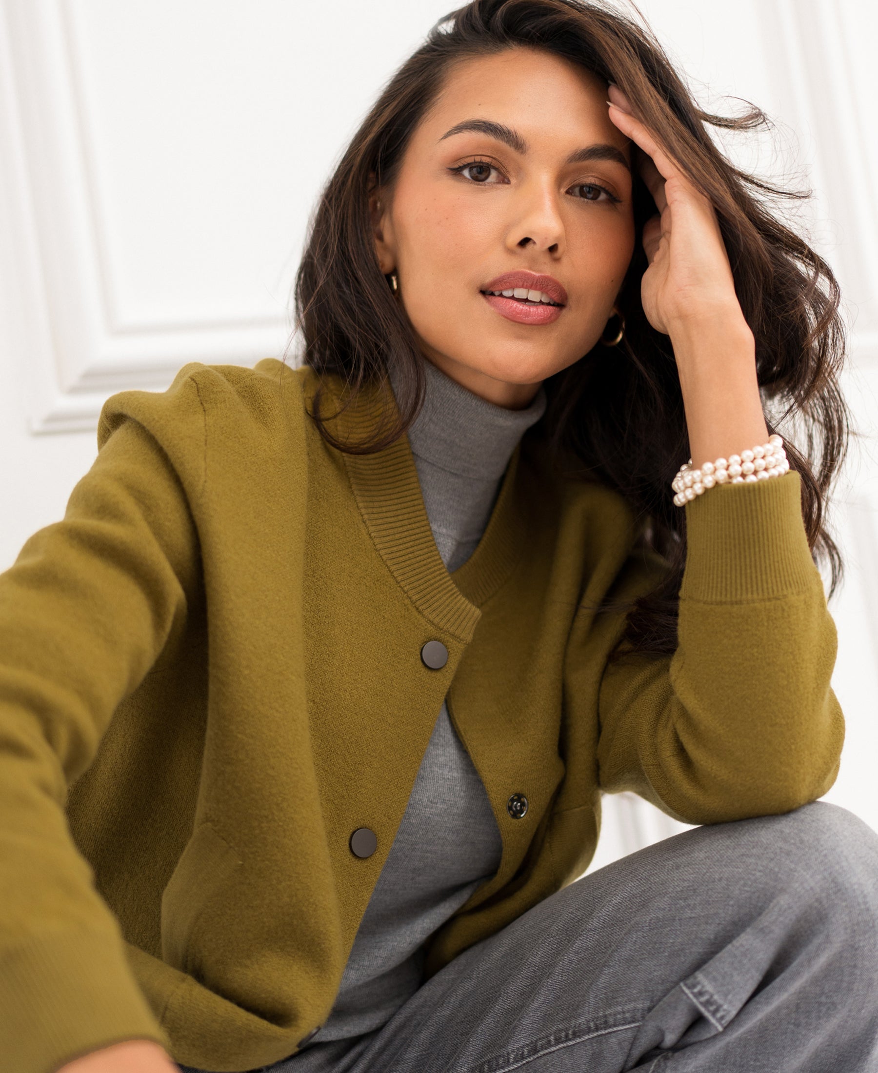 Woman wearing an olive green bomber jacket sits indoors.