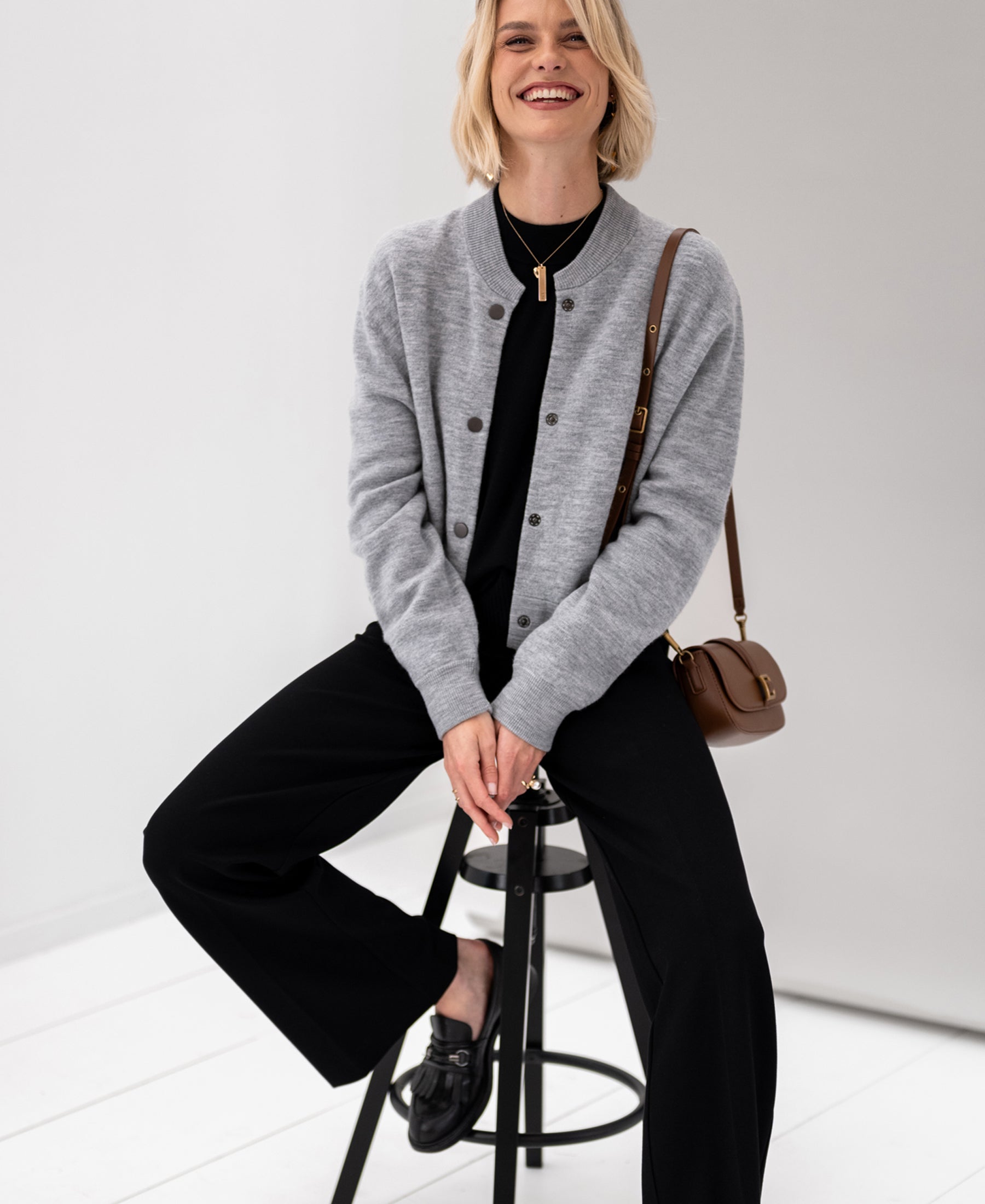 Woman wearing PLEIN PUBLIQUE's LA BOMBA grey melange bomber jacket sits, shown from the front.