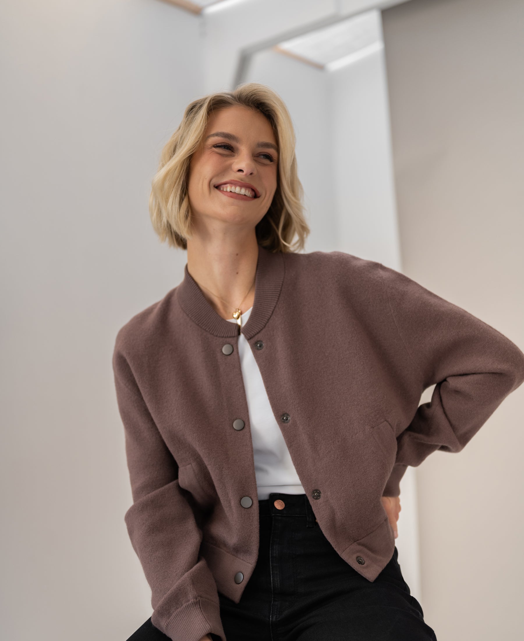 A woman with short blonde hair smiles, wearing a PLEIN PUBLIQUE bomber jacket called LA BOMBA Innuendo.