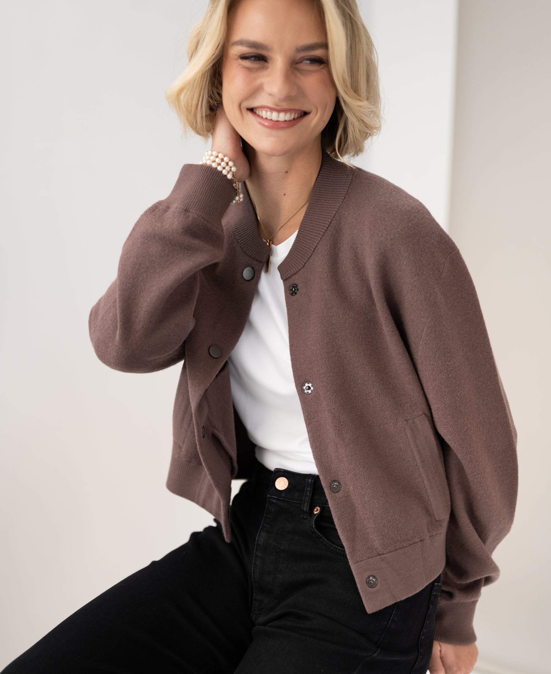 Woman wearing a PLEIN PUBLIQUE bomber jacket, sitting sideways.