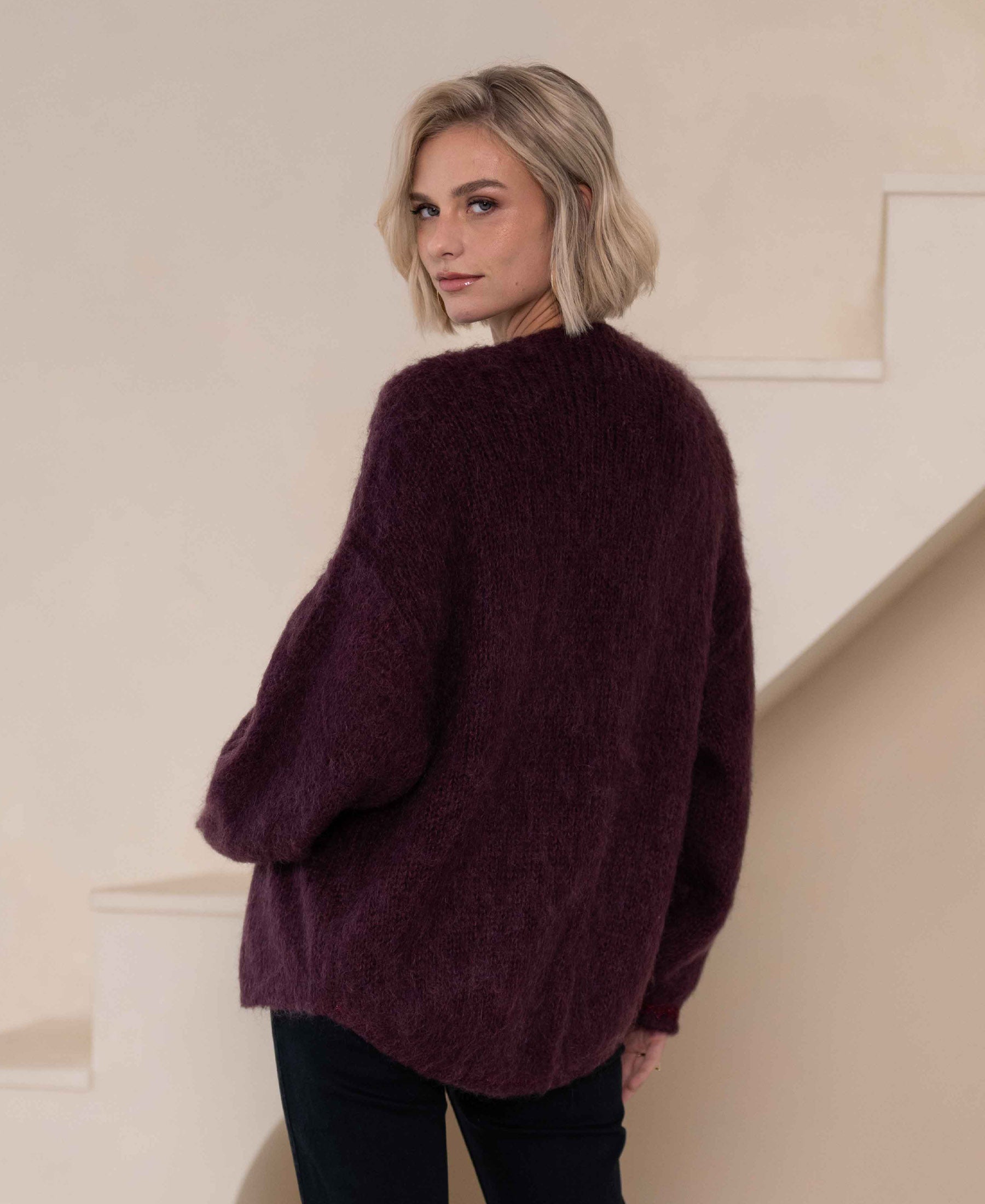 Bordeaux fluffy vest called LA CHERIE by PLEIN PUBLIQUE shown in front of a beige staircase.