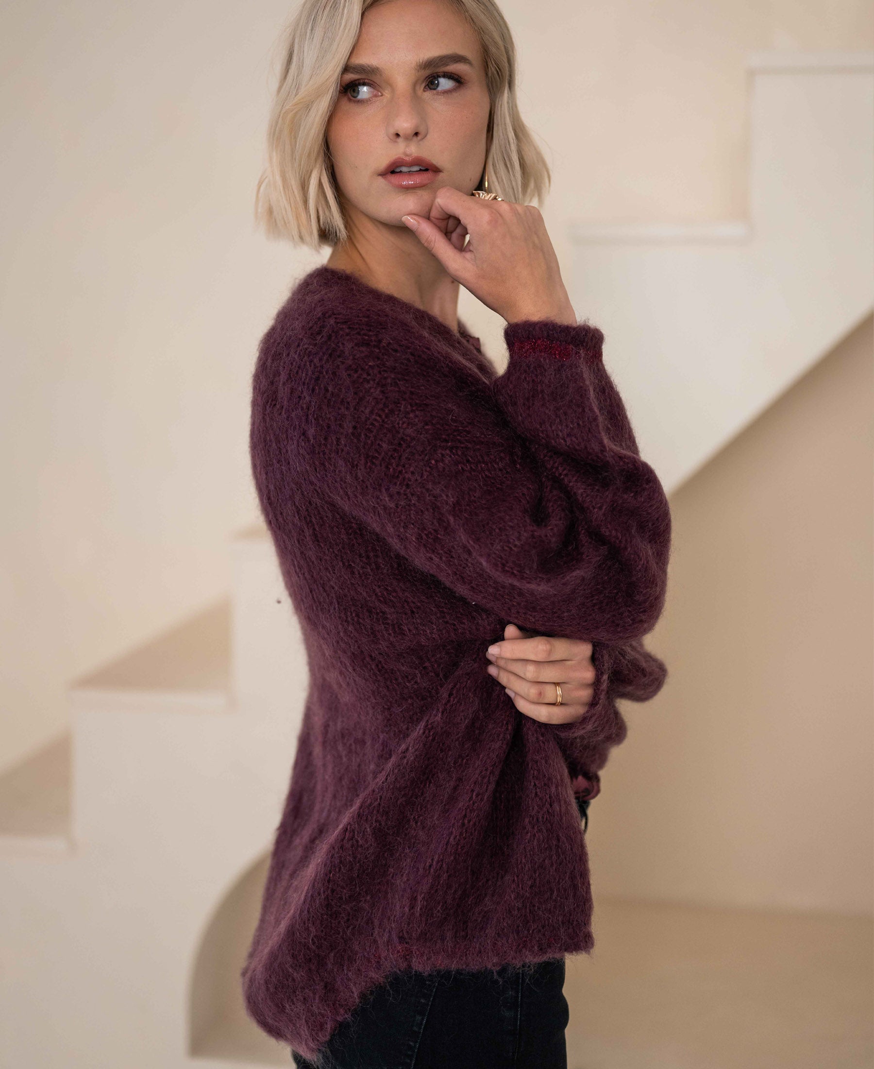 A woman with short blonde hair wears the PLEIN PUBLIQUE Fluffy LA CHERIE vest in Bordeaux by light stairs.