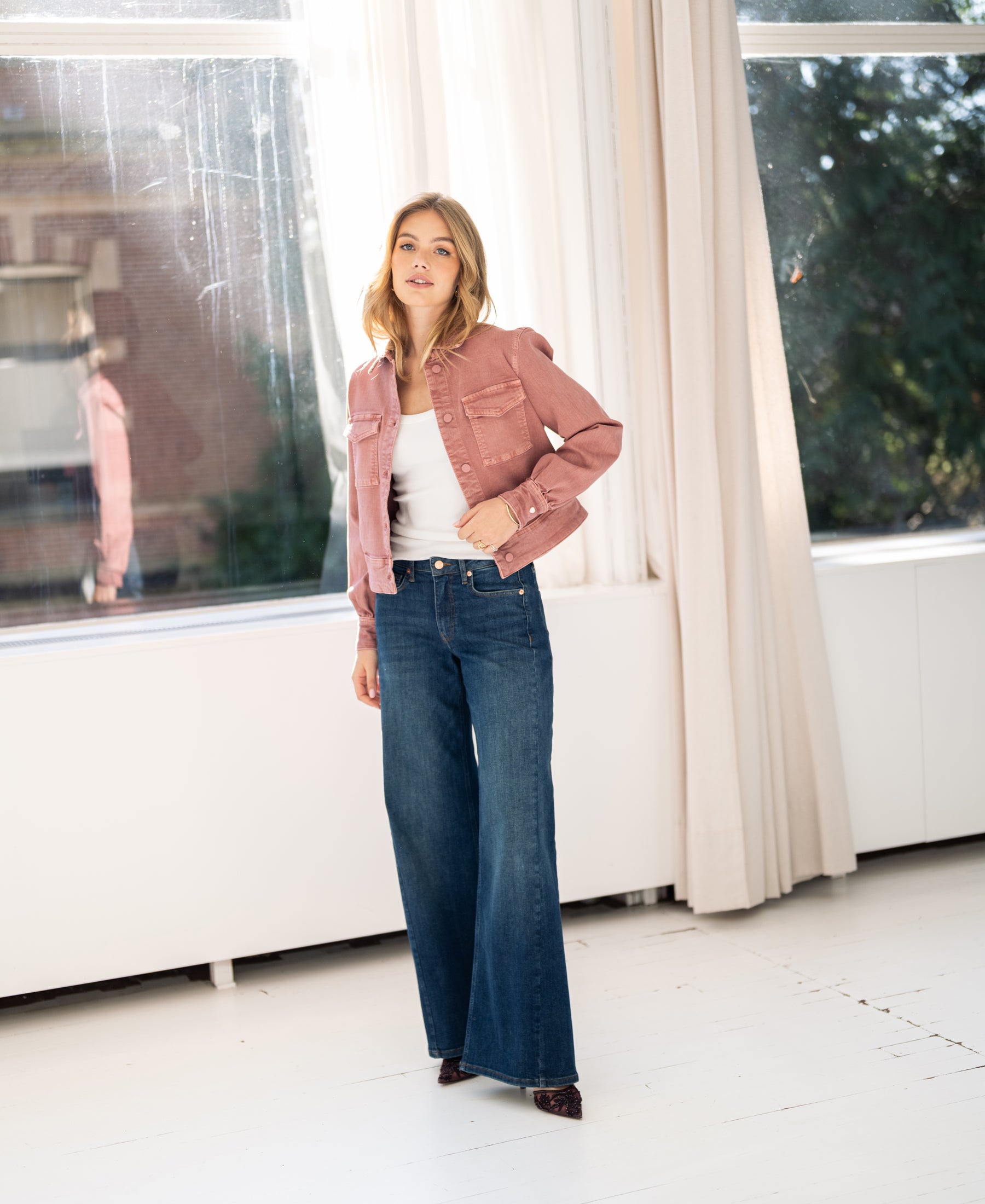 Woman wears a dusty pink stretch denim jacket in a bright room.