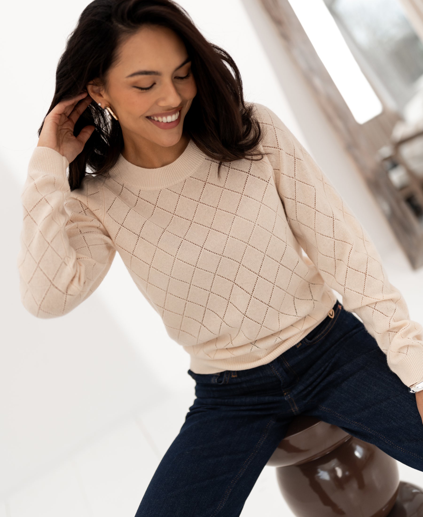 Woman wearing a PLEIN PUBLIQUE Argyle merino wool sweater in butter yellow, seated, front view.