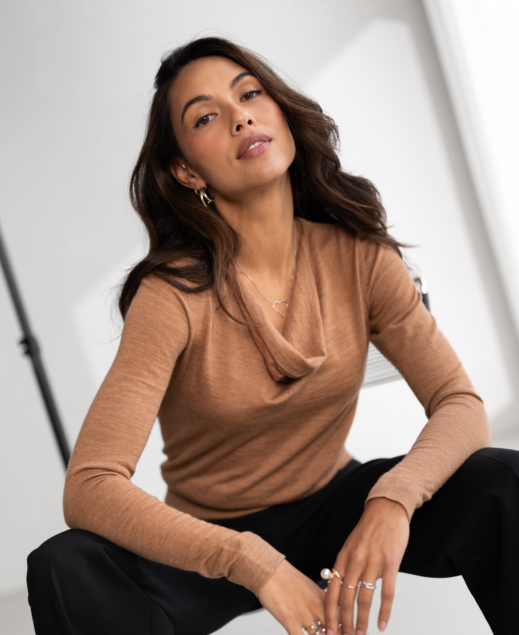 Chai tea-colored waterfall-neck sweater with long sleeves, shown on a model seated indoors.