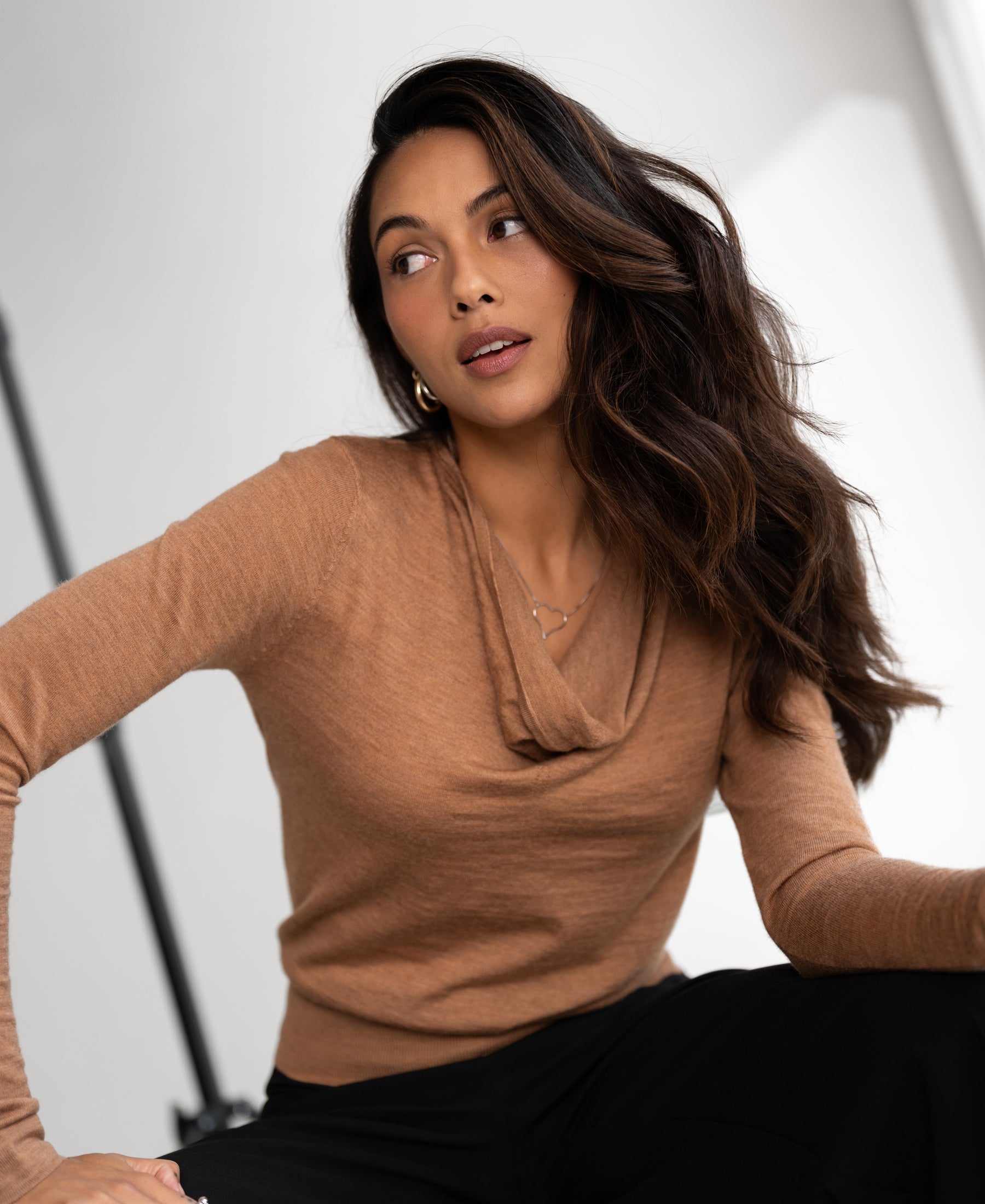 Chai tea colored waterfall neck sweater in soft knit, shown indoors on a model with long wavy hair, side view.