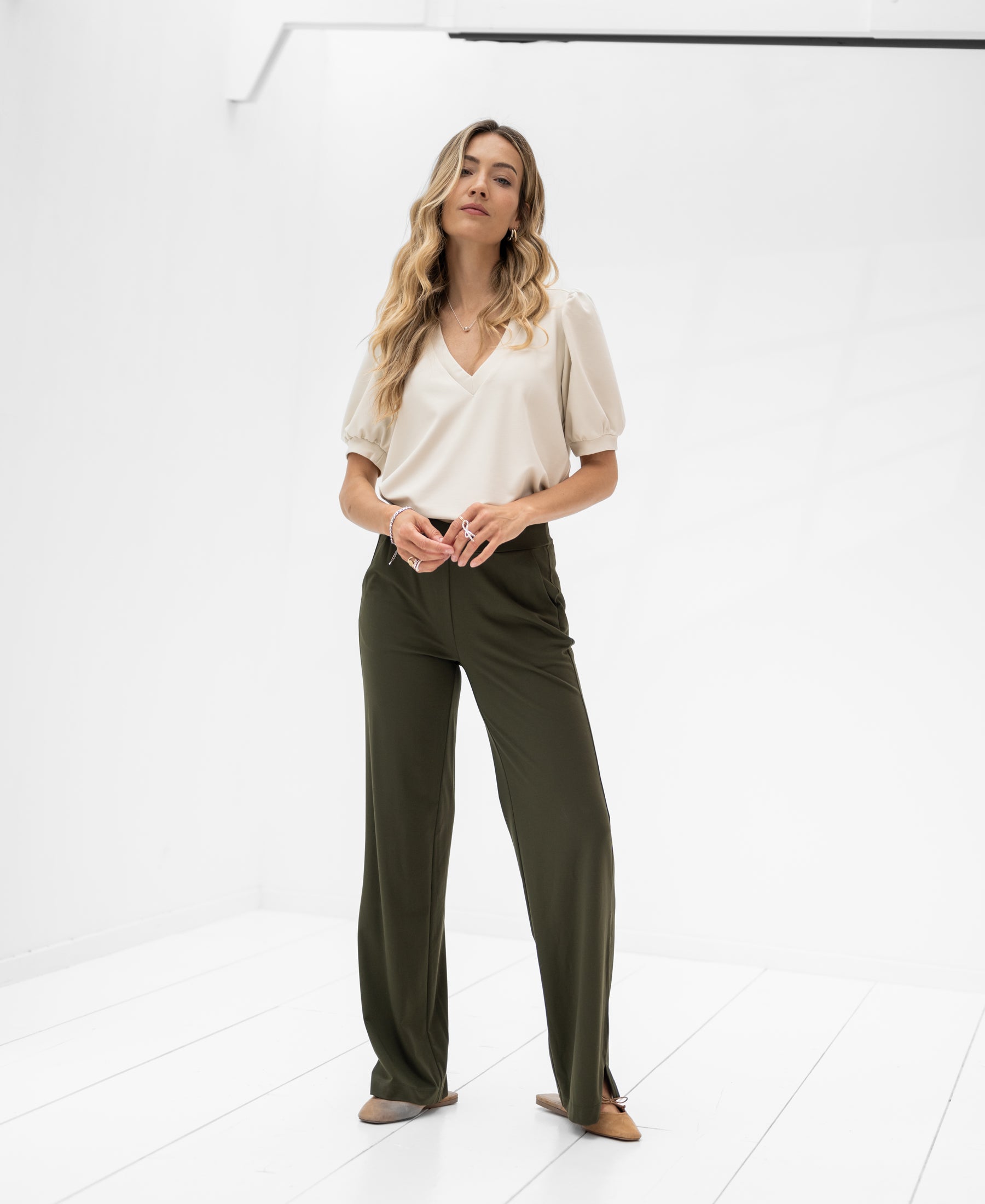 Front view of a woman wearing a stone-colored LA CELINE Traveltop by OVERIG in a bright white room.