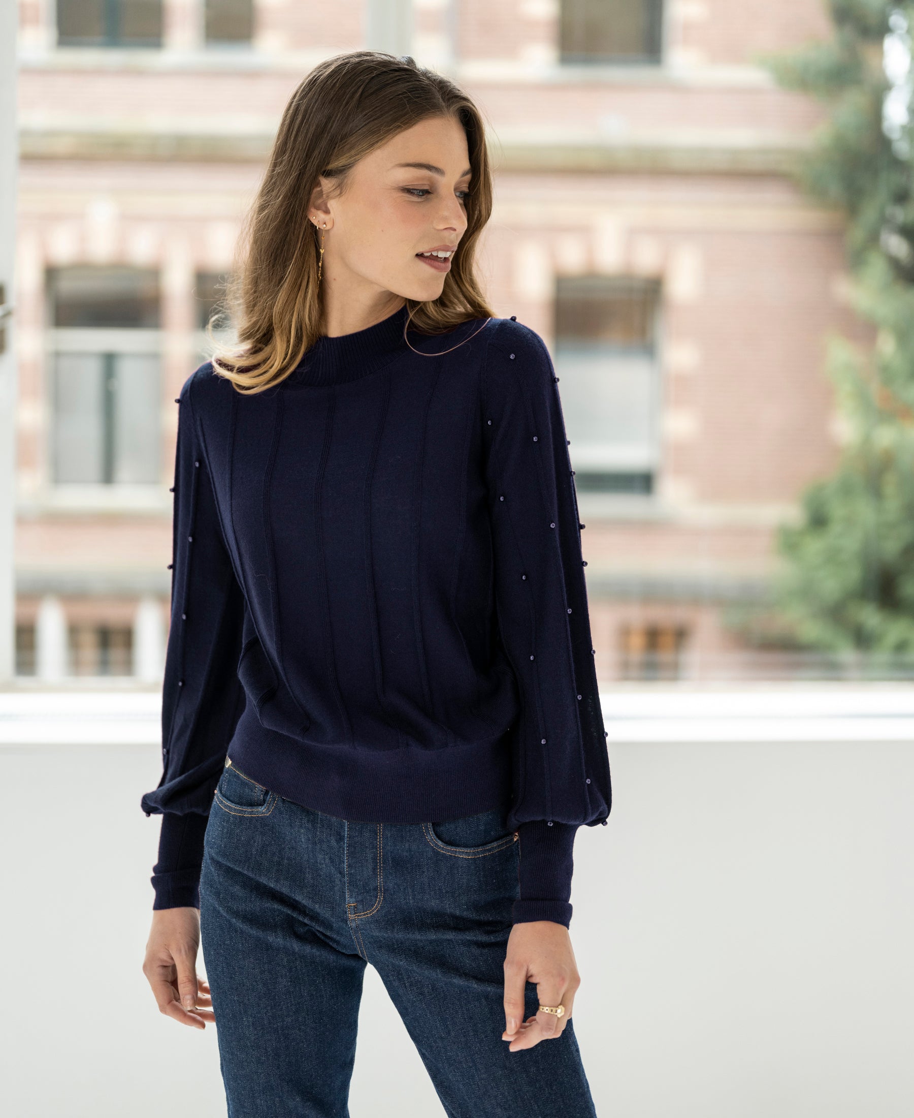 Woman wearing a PLEIN PUBLIQUE navy blue turtleneck sweater with beaded details.