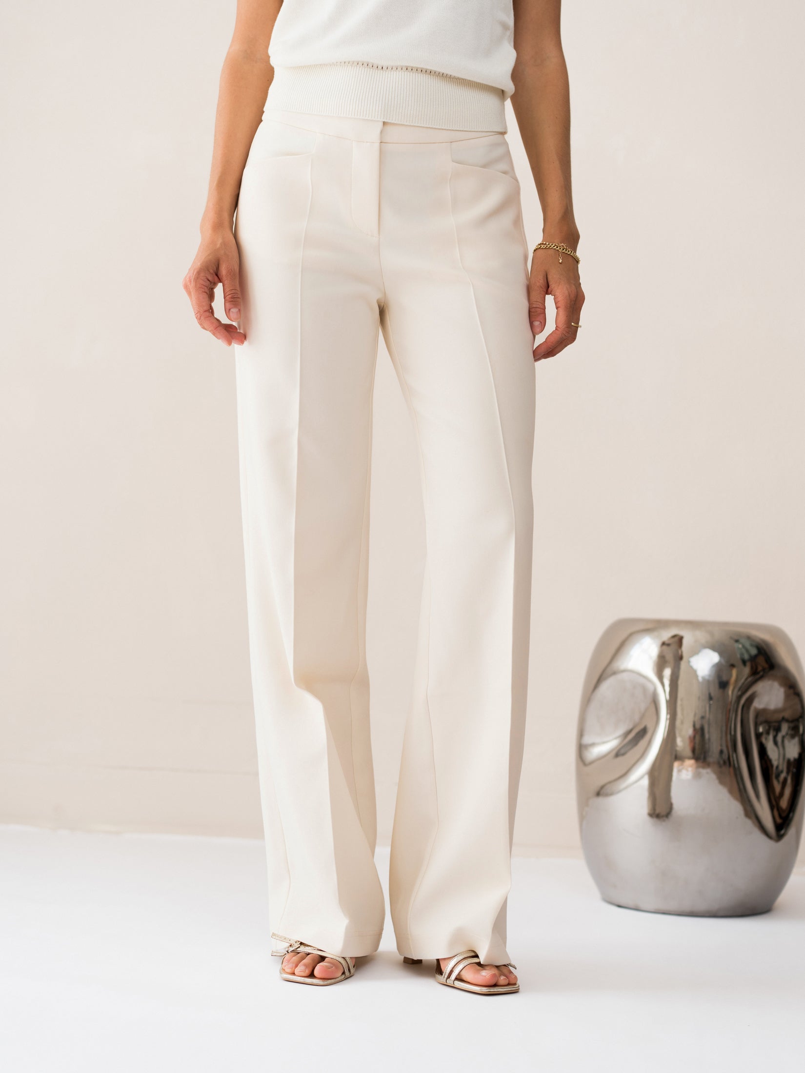 Woman wearing cream wide-leg pants stands, shown from the side.