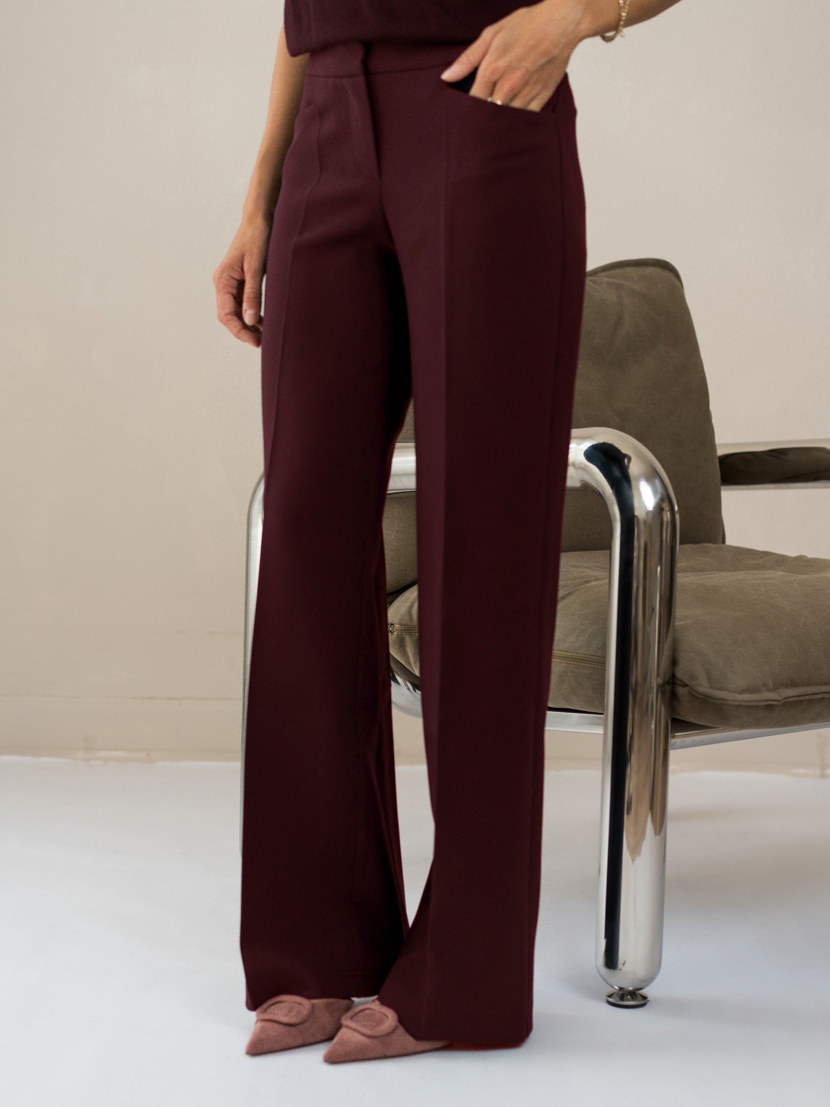 Woman wears wide-leg pants in Bordeaux color by a modern metal chair.
