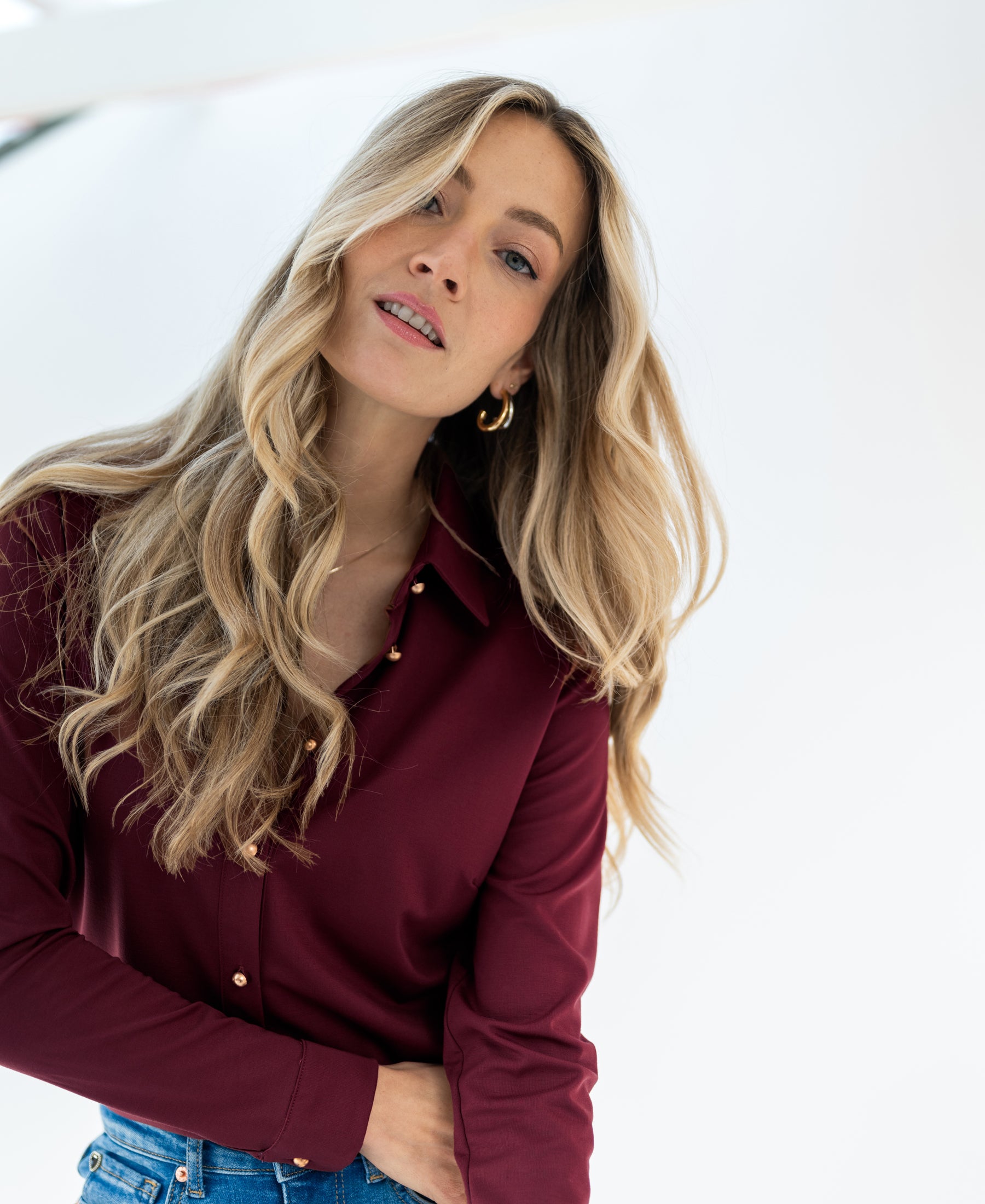 Woman wearing a Plein Publique travel blouse in cherry wine color stands against a white background.