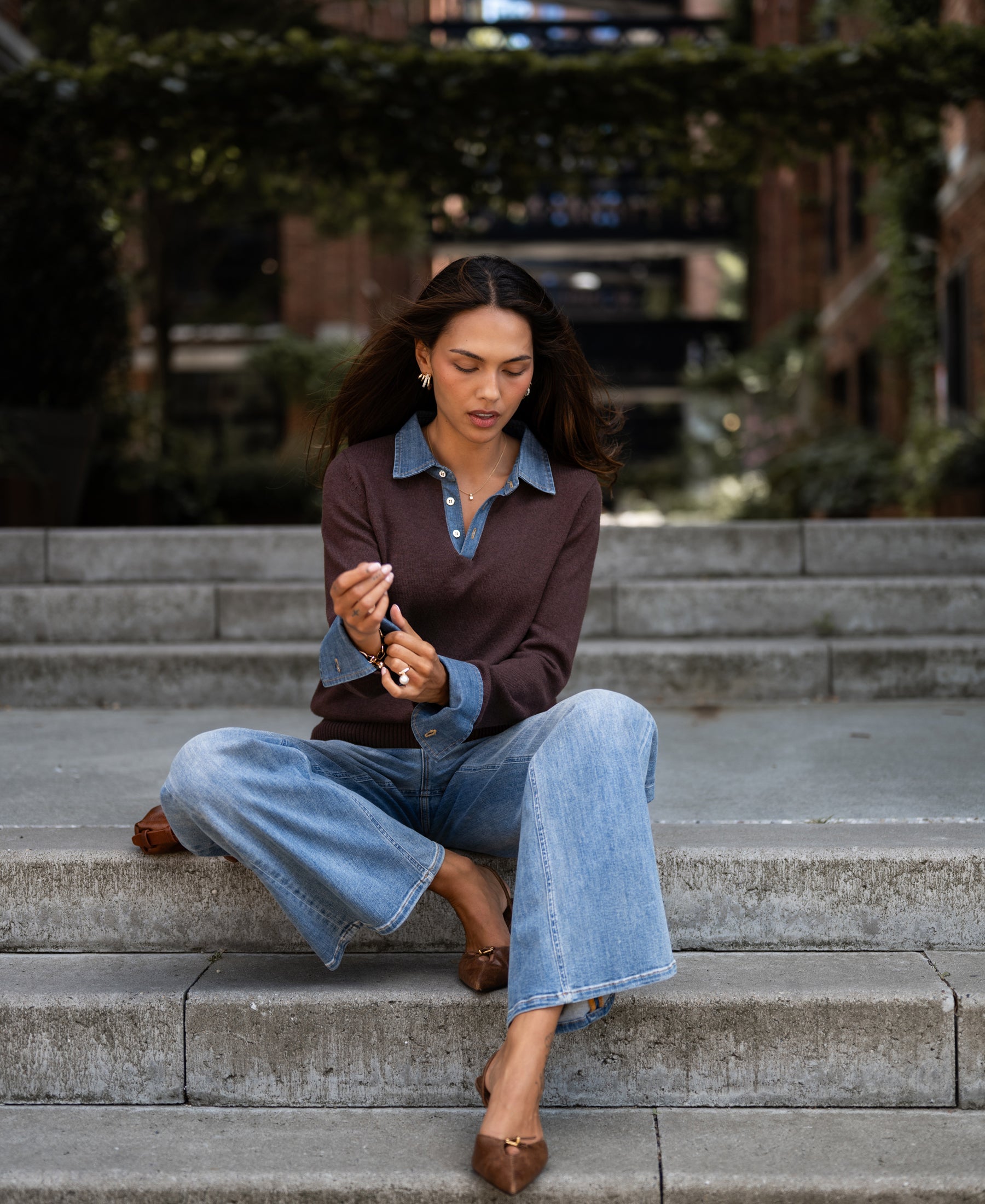 Woman sits on outdoor steps wearing a Pure chocolate brown sweater-blouse, looking down.