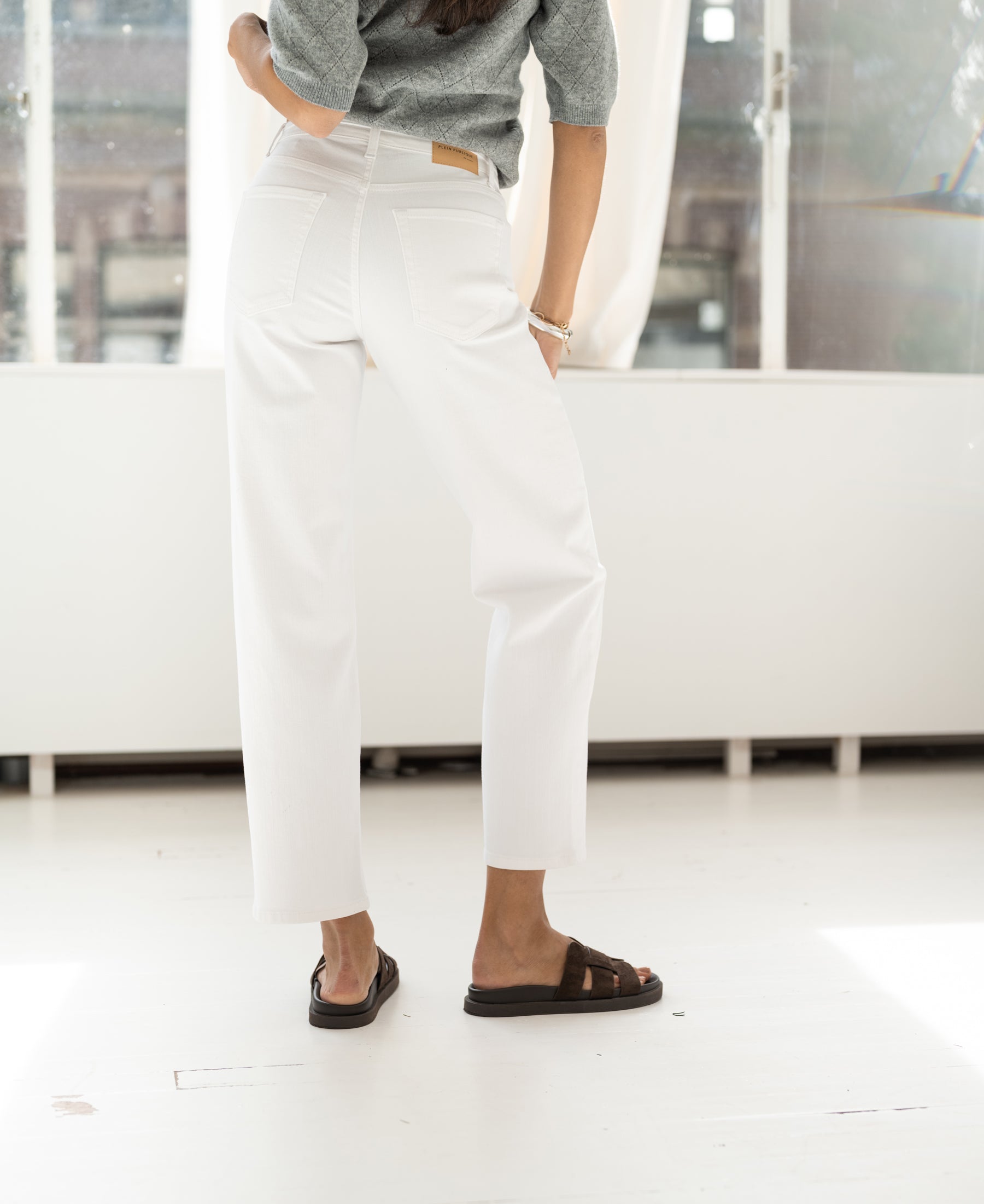 White cropped jeans shown indoors near a bright window.
