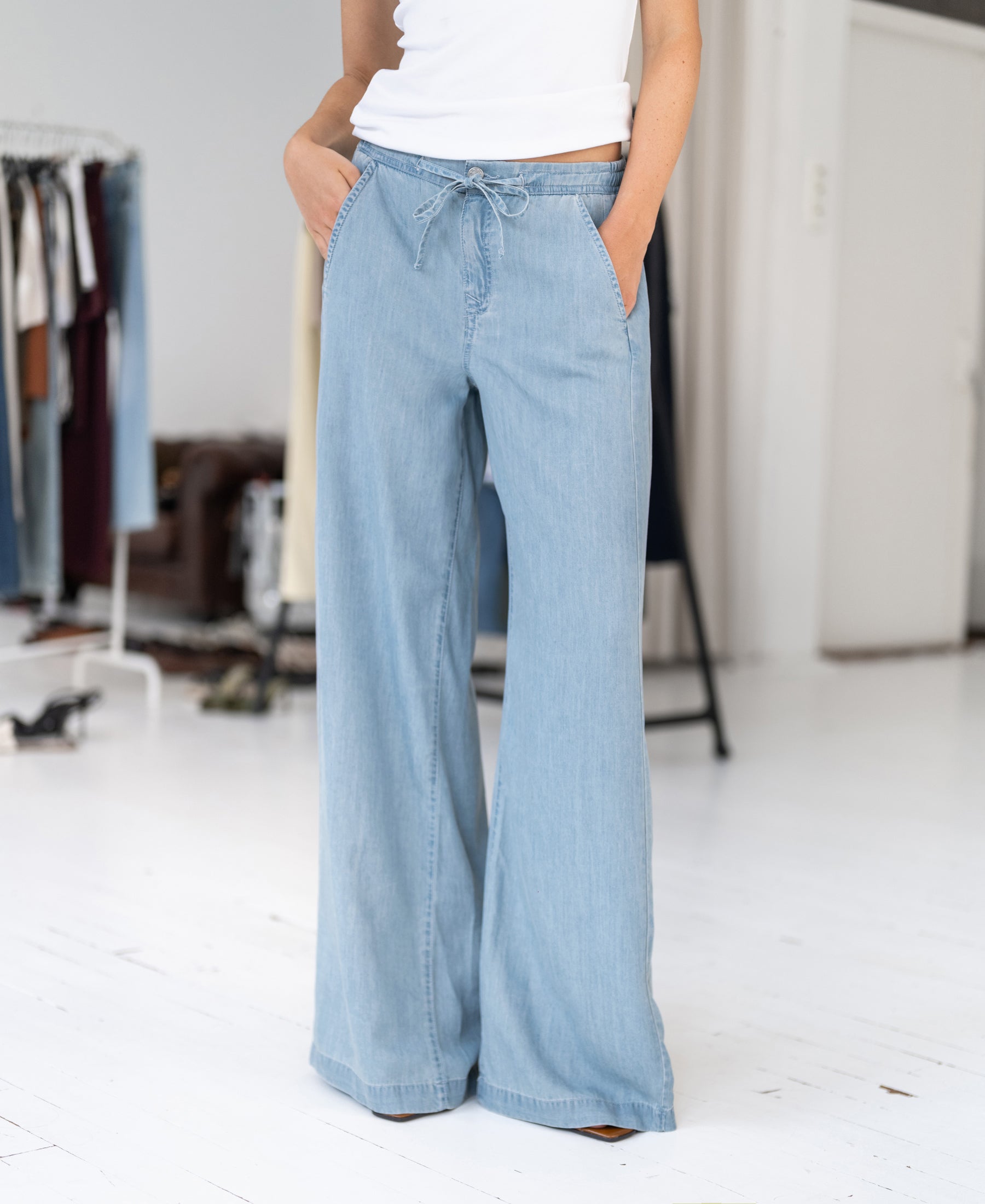 Person wears bleached Tencel denim jeans by PLEIN PUBLIQUE in a bright room with clothing racks.