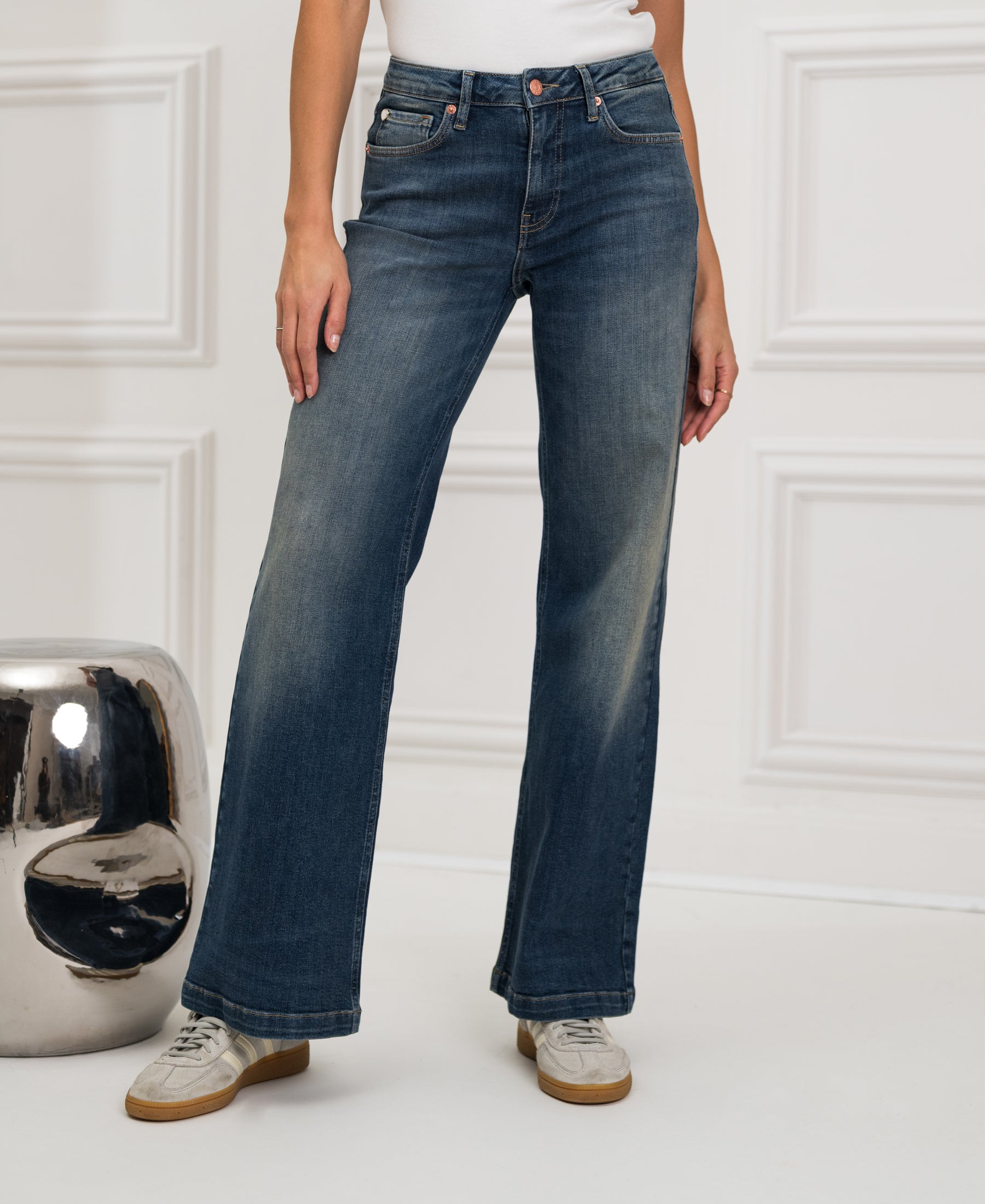 Blue vintage wide leg jeans in an indoor setting, shown next to a reflective silver stool.