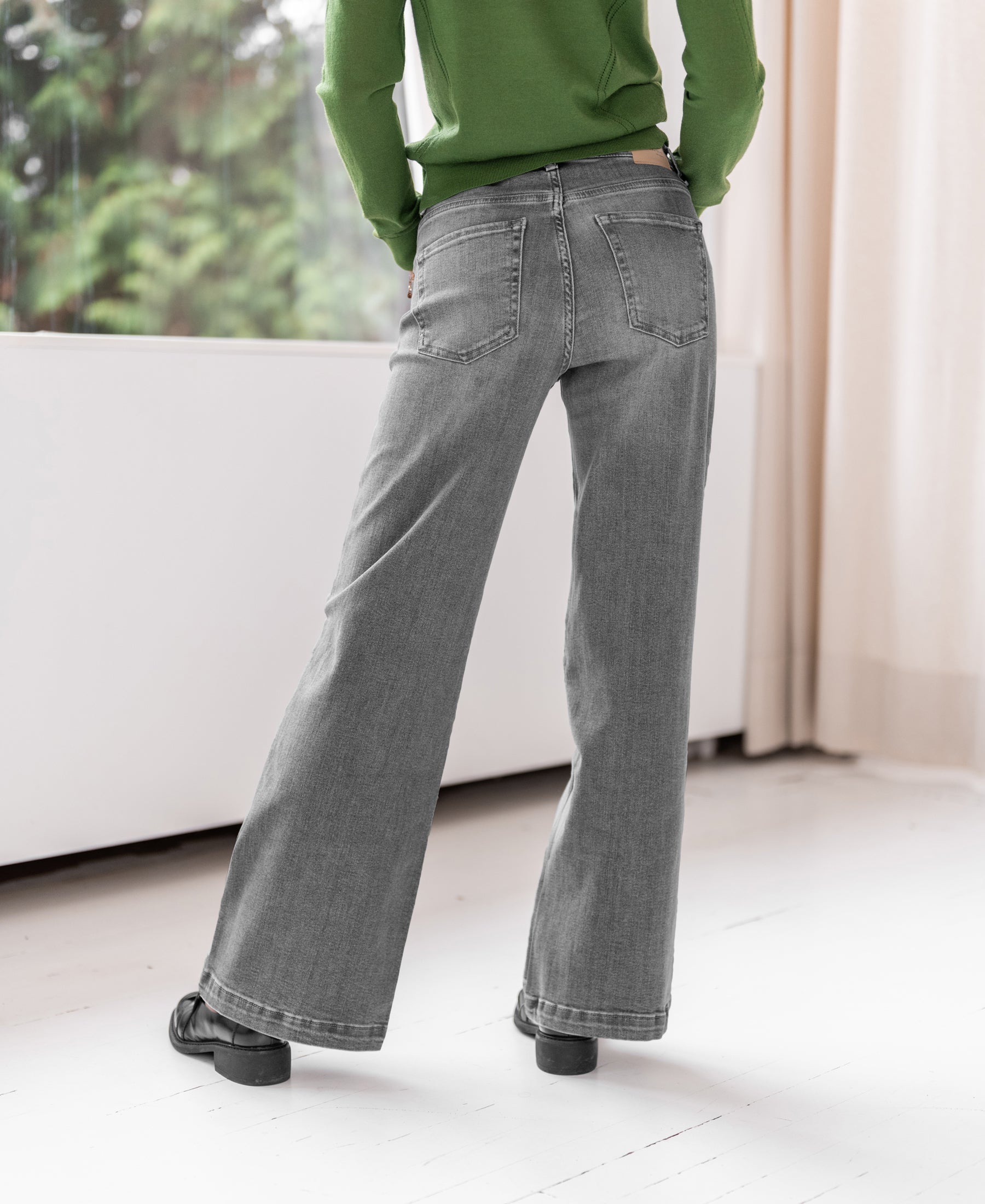 Wide leg jeans in grey stonewash displayed indoors by a bright window.