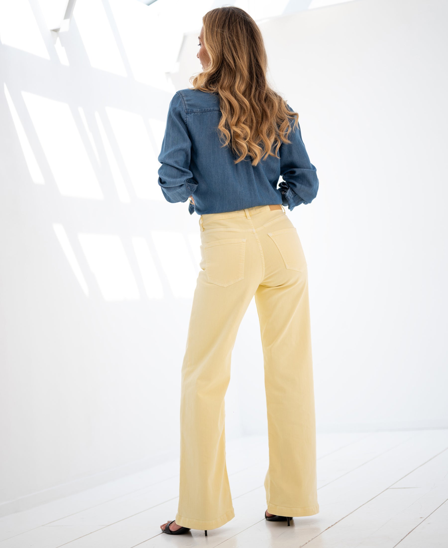 Woman indoors in bright light wears wide leg jeans in soft yellow.