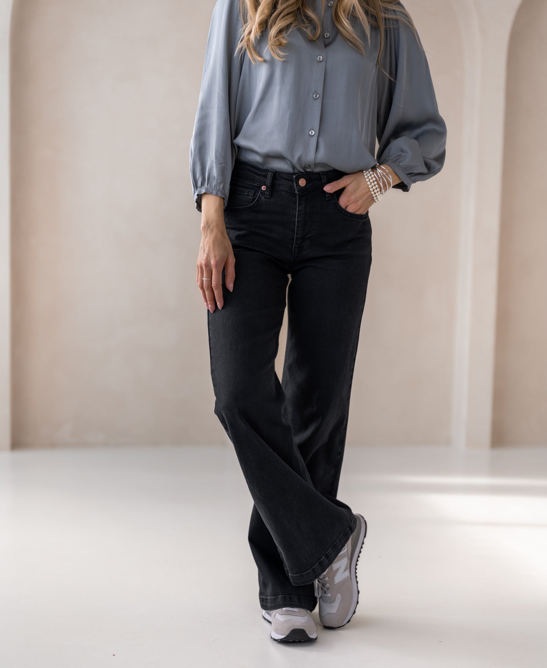Woman wearing wide leg black denim jeans, standing indoors in a relaxed pose.