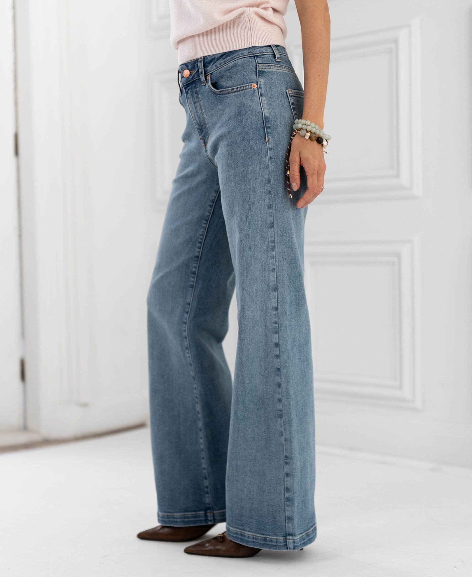 Woman wearing wide leg jeans in light stone wash, standing on a white floor.