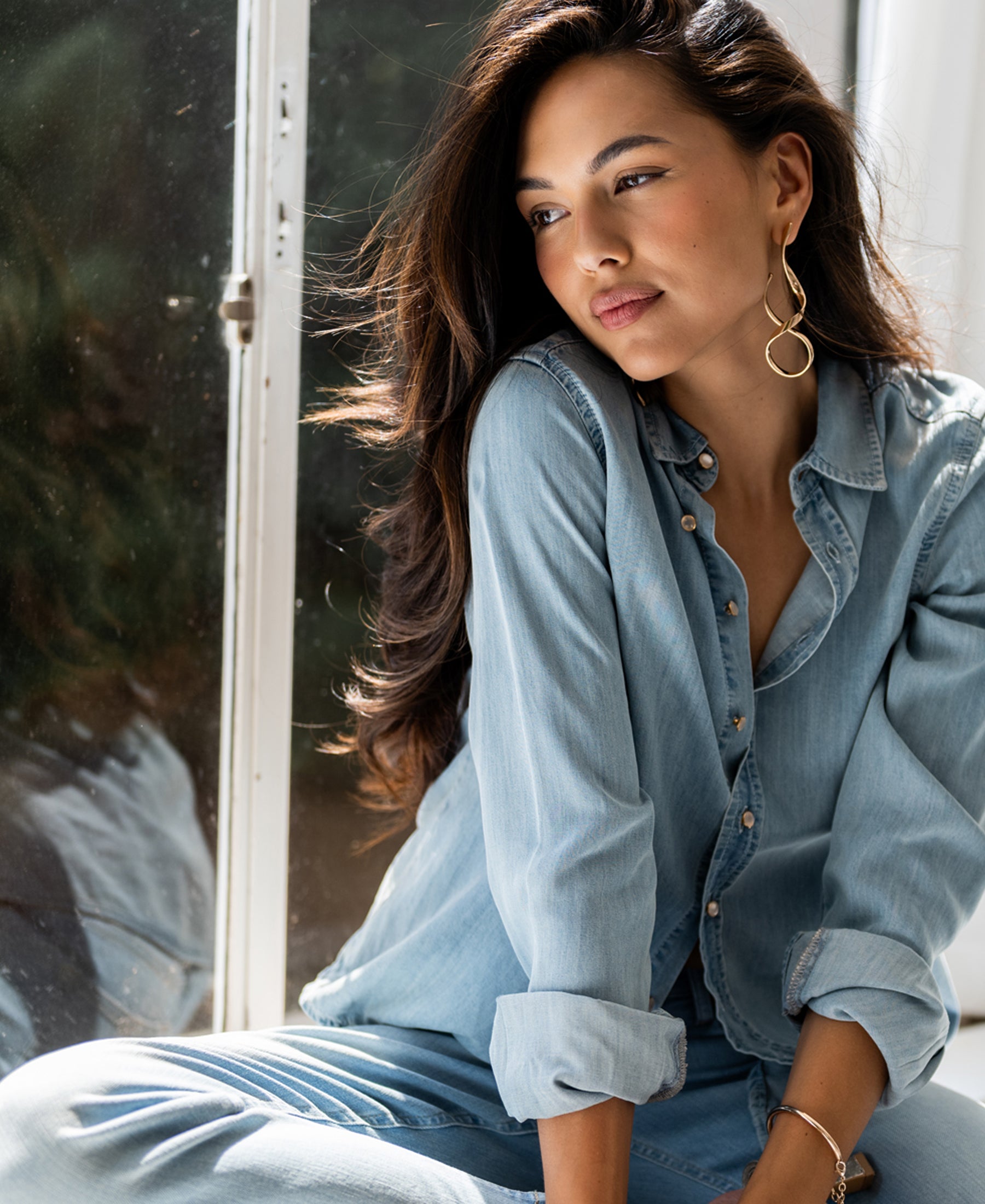 Bleached Tencel denim blouse in light blue, shown worn by a woman seated indoors.