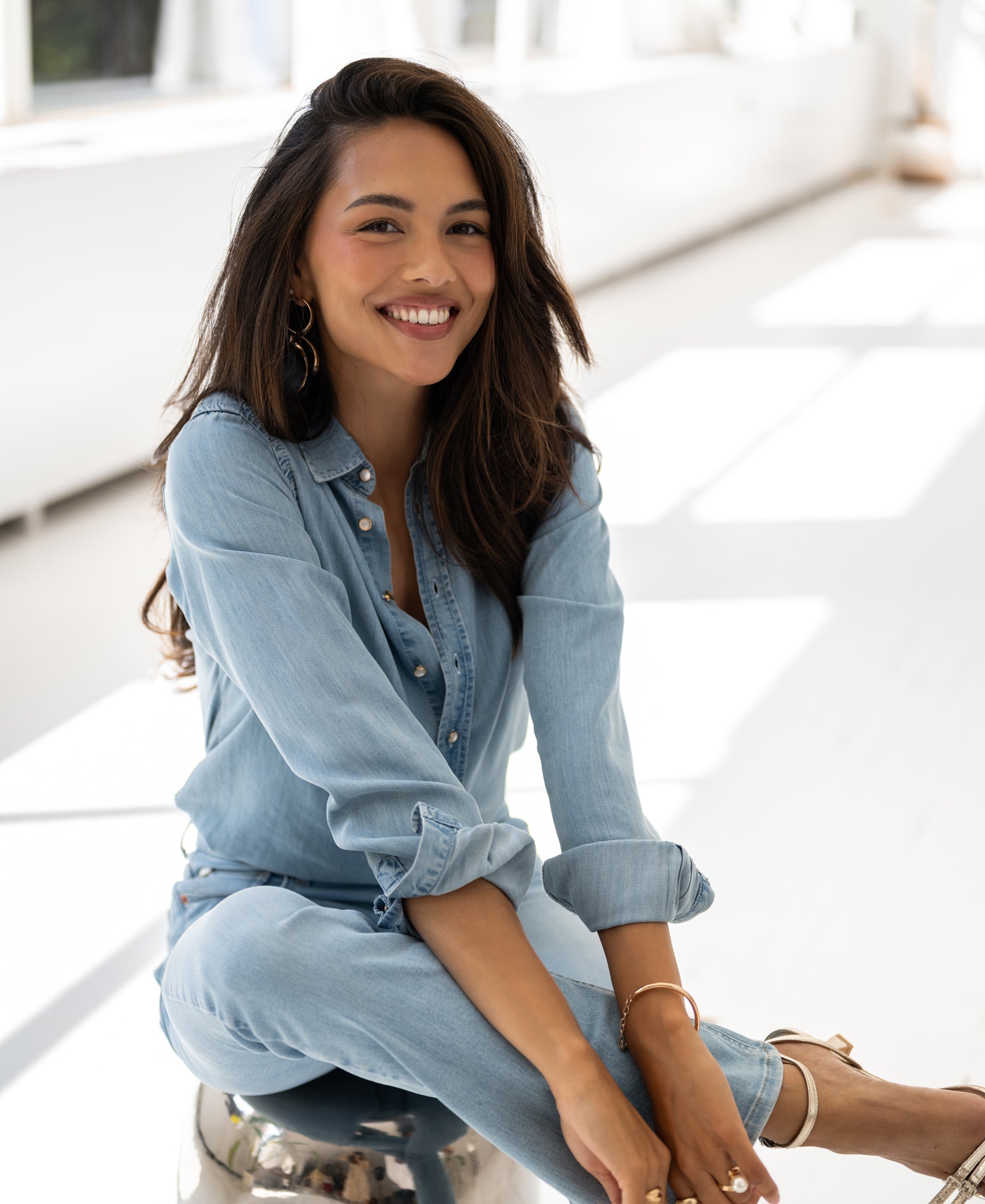Tencel denim blouse in bleached blue, shown worn by a woman seated in a sunlit room.