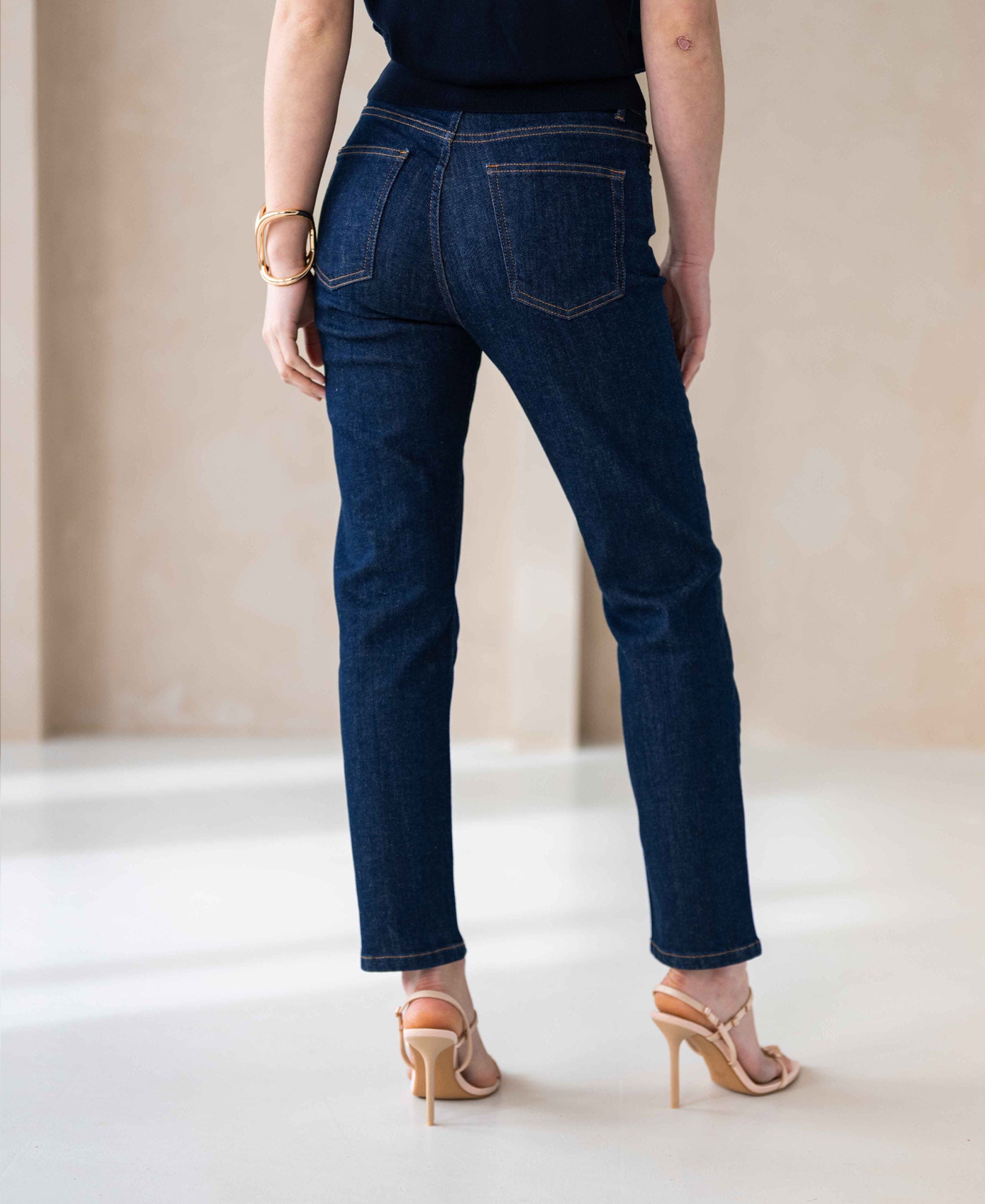 Back view of person wearing cropped blue rinsewash jeans, indoors.