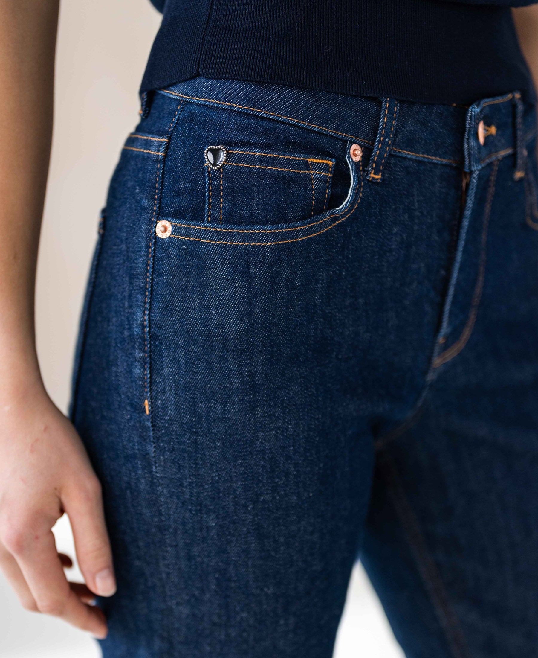 Waist-down view of person wearing dark blue cropped jeans in stretch denim, rinse-wash finish.