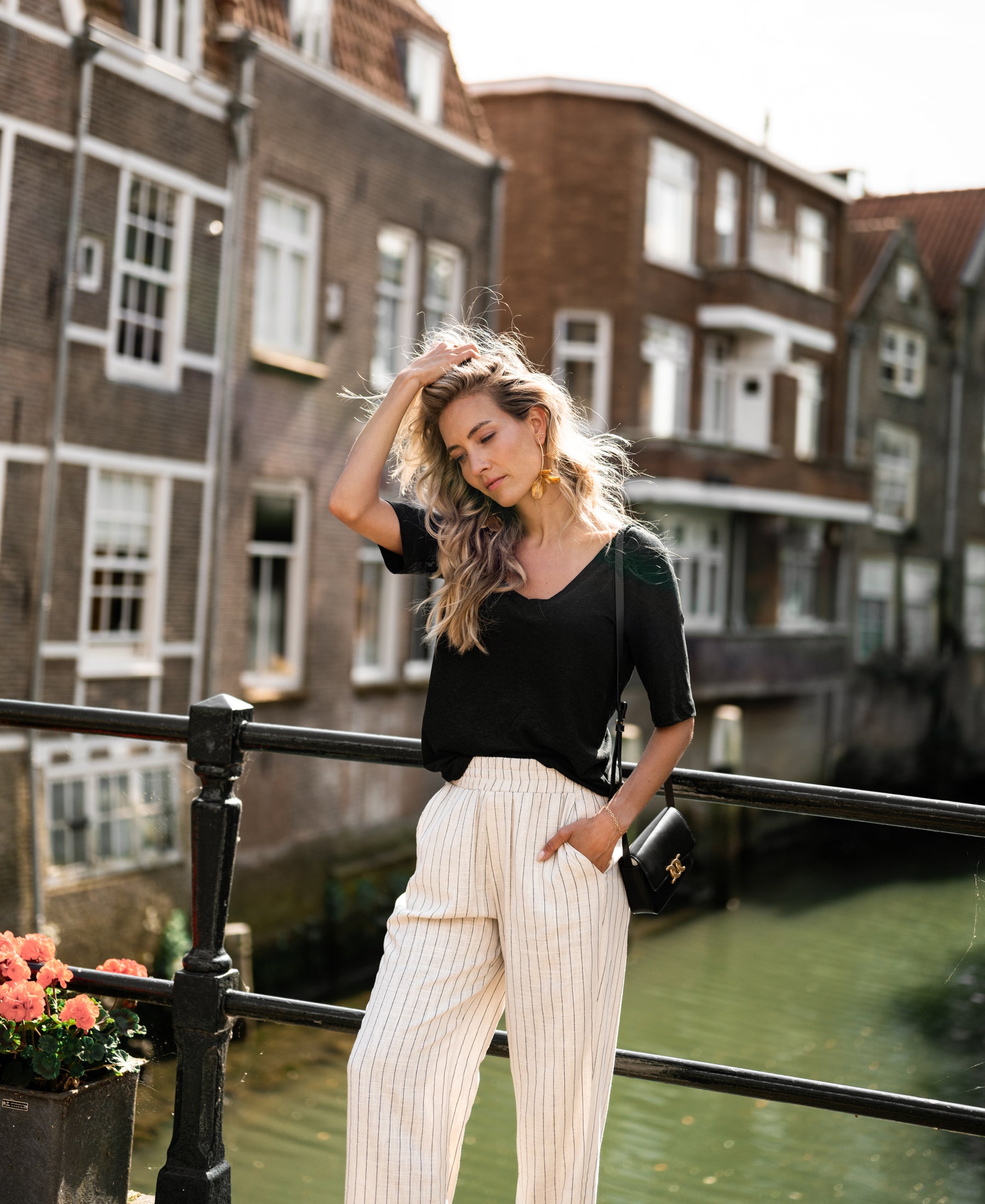 Woman wearing a black LA DOMI linen T-shirt by PLEIN PUBLIQUE, standing outdoors.