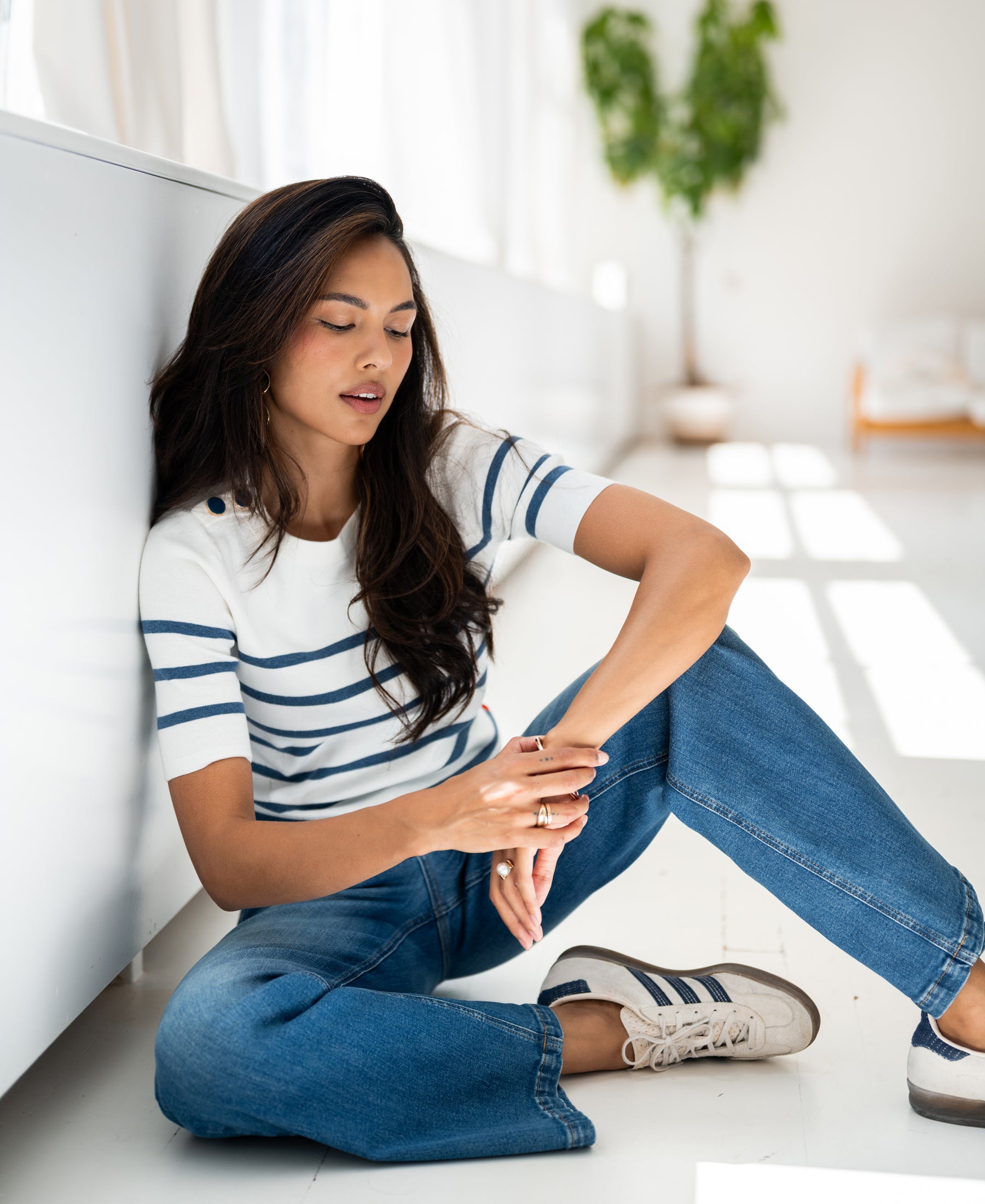 Woman wearing PLEIN PUBLIQUE Breton striped sweater ESISA in ivory and denim blue, sitting indoors in sunlight.