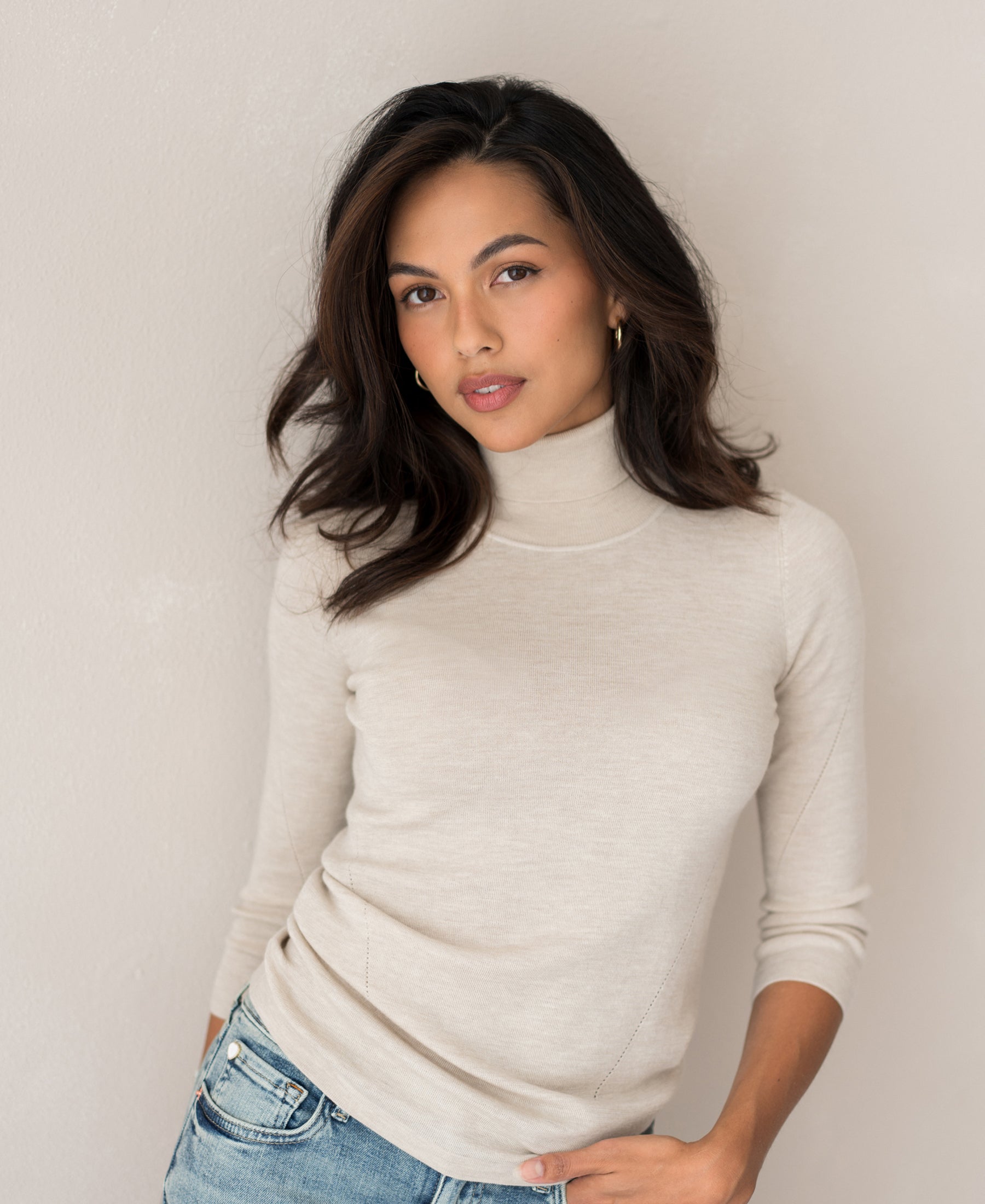 Woman with long dark hair wears the LE FABIAN Beige Turtleneck Sweater by PLEIN PUBLIQUE.