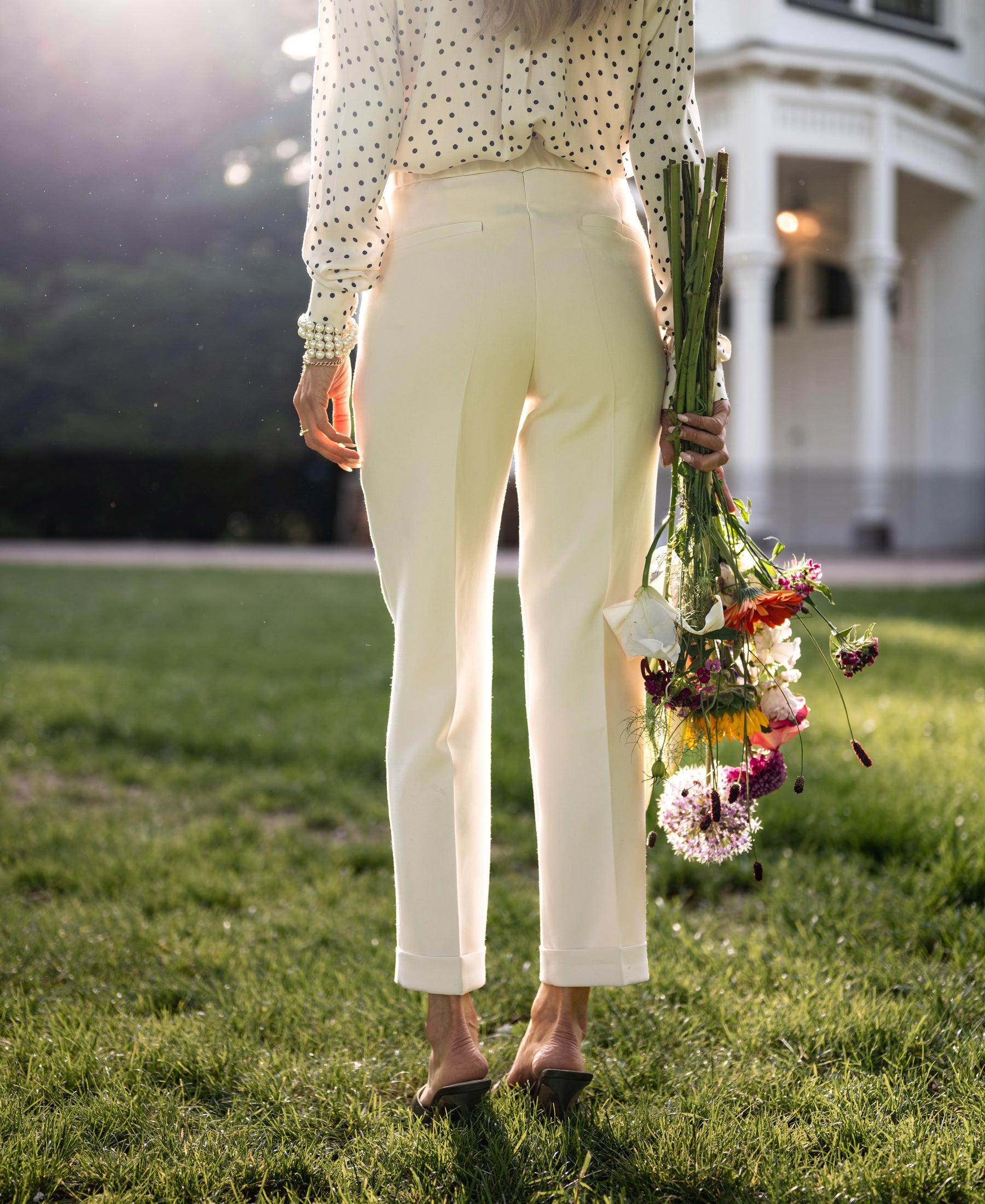 Cream cropped pants shown on a woman standing on grass near a white building.