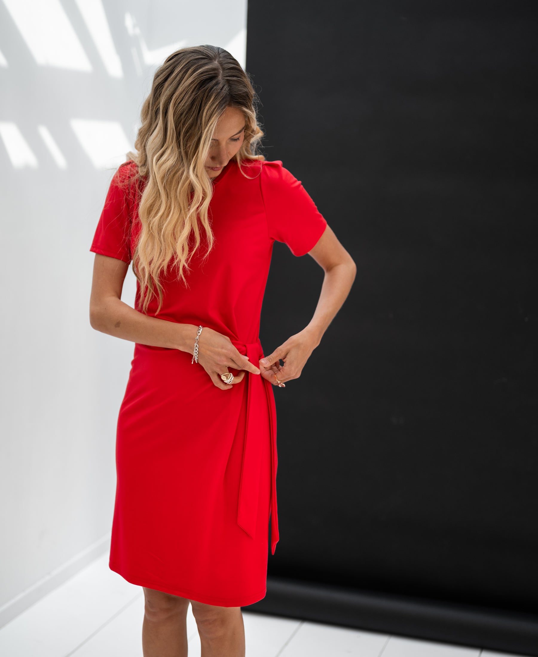 Red wrap dress with waist belt tied at the front, shown against a black and white background.