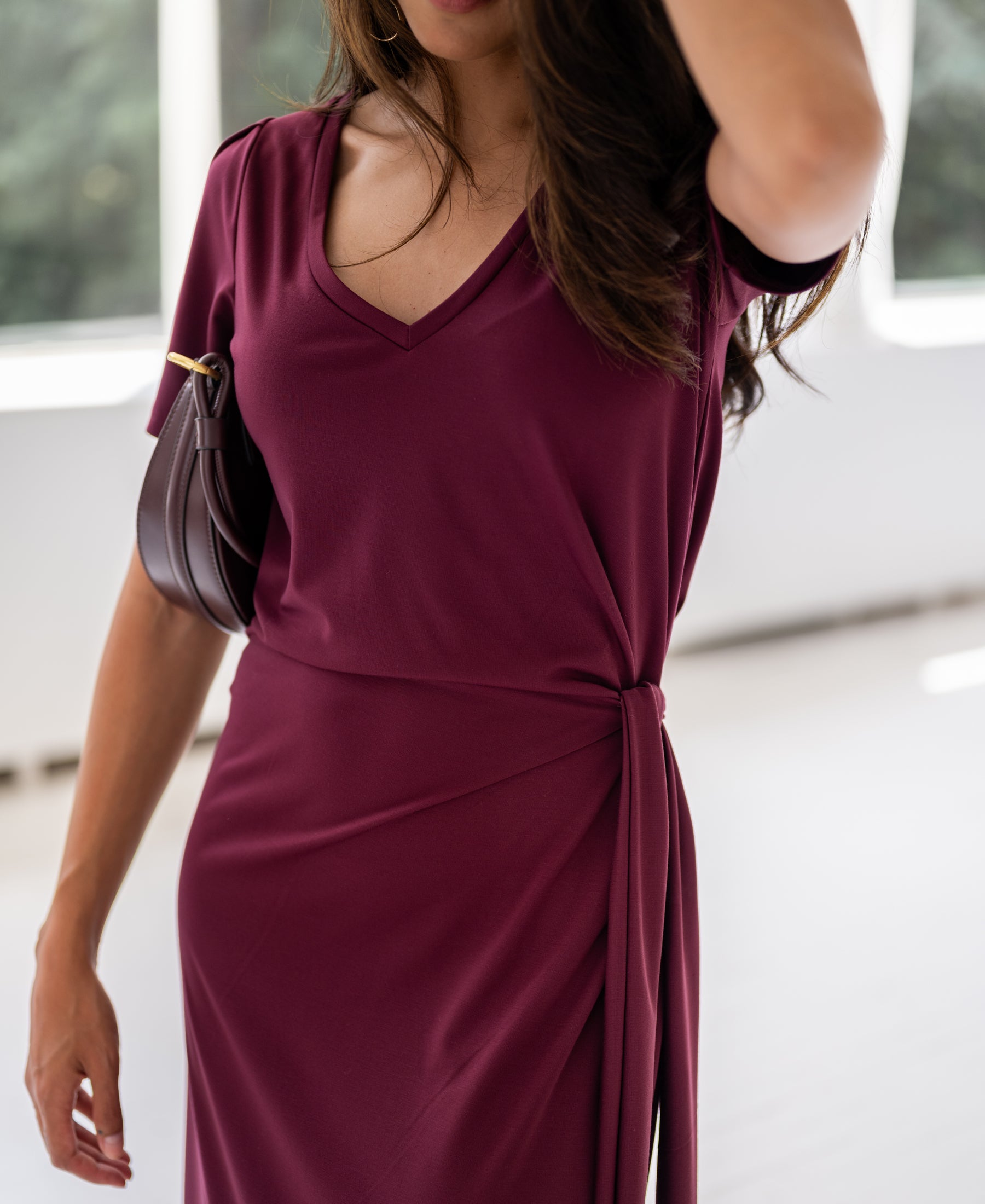 Woman wearing a wine-colored PLEIN PUBLIQUE long dress with v-neck, indoors.
