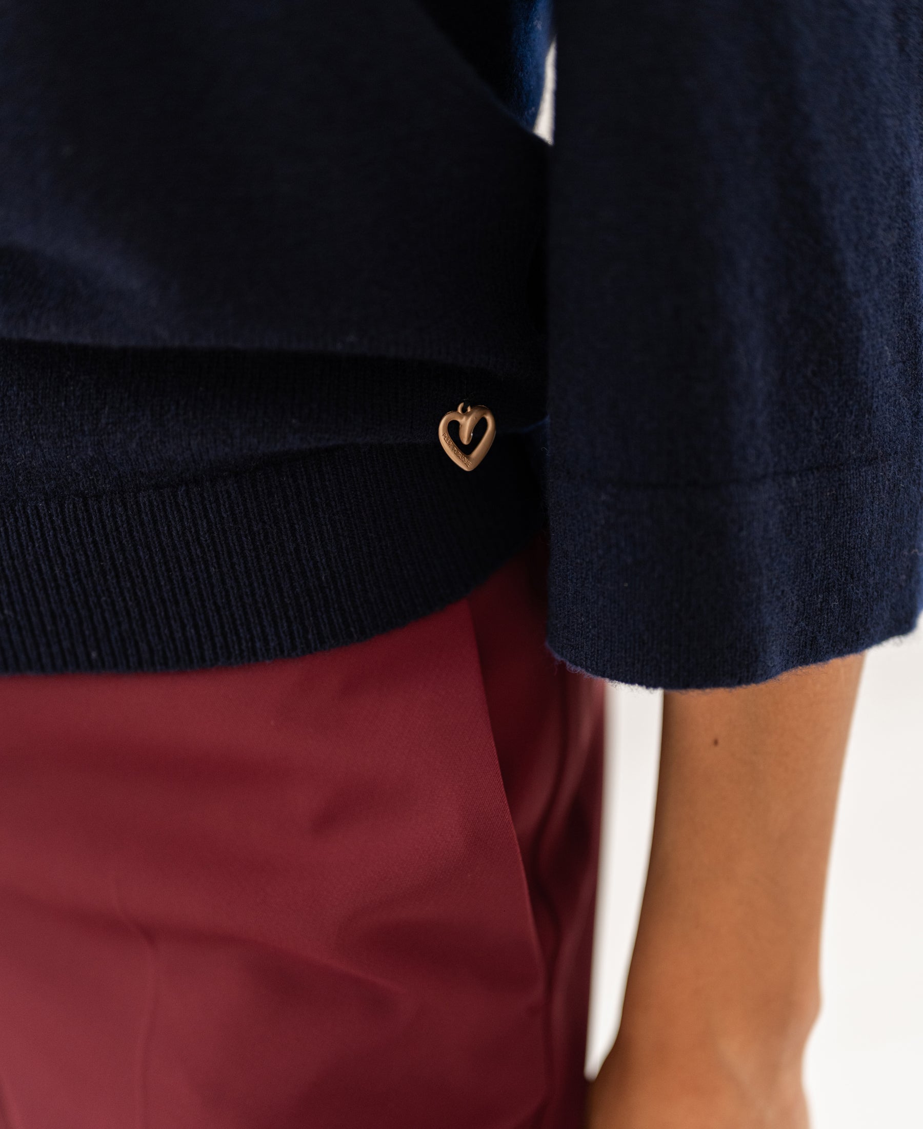 Person wearing the PLEIN PUBLIQUE LE FREJUS dark blue merino wool sweater with a gold heart charm.