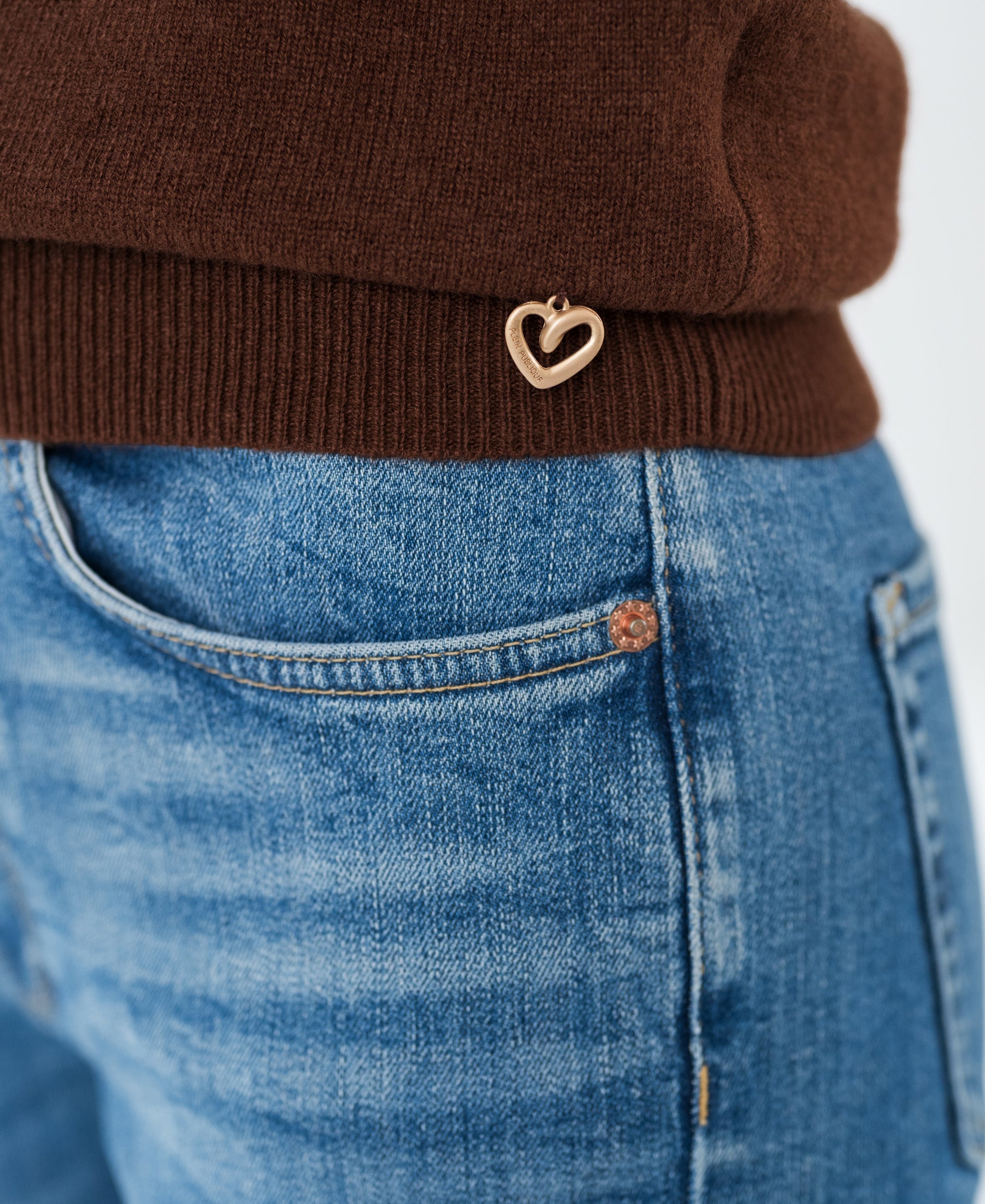 Close-up of the cacao-colored Merino wool sweater with a gold heart charm near the hem.