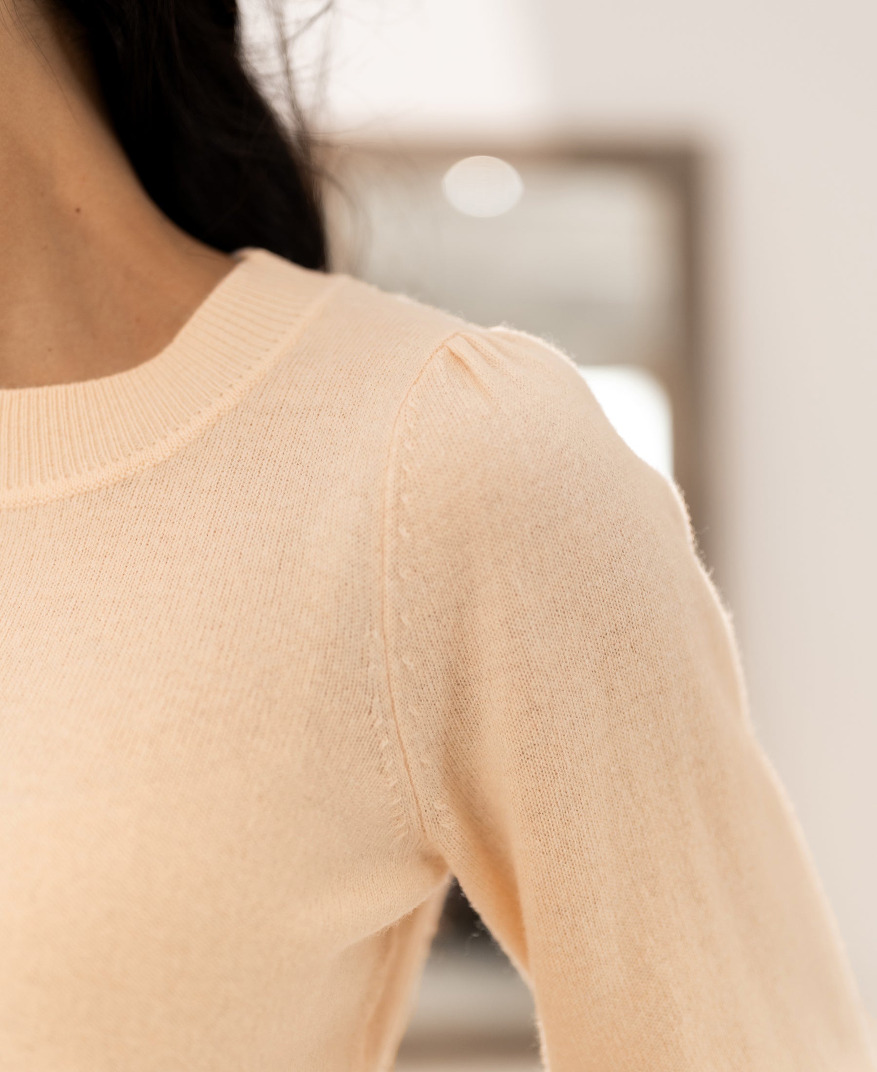 Close-up of a merino wool sweater in butter color with a round neck and long sleeves.