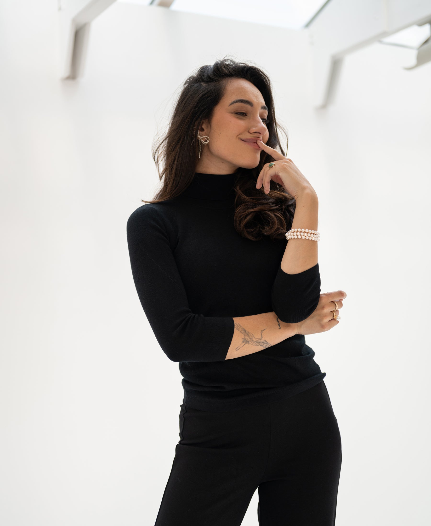 A woman wears a black LE FABIAN turtleneck sweater by PLEIN PUBLIQUE indoors, posing and smiling.