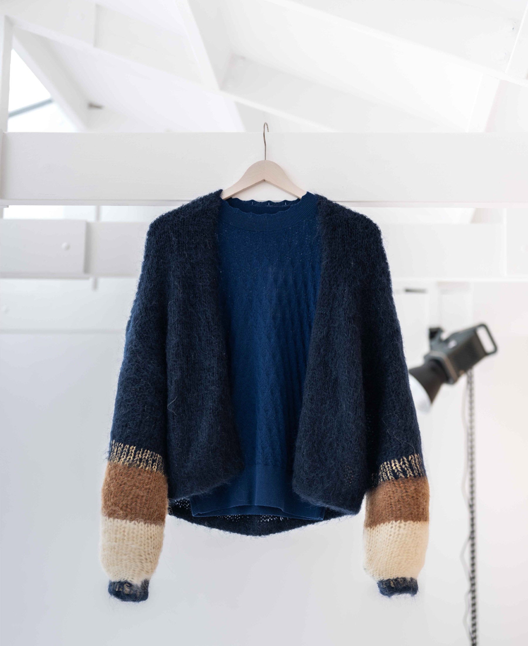 The PLEIN PUBLIQUE fluffy vest in dark blue with stripes hangs in a bright, modern room.