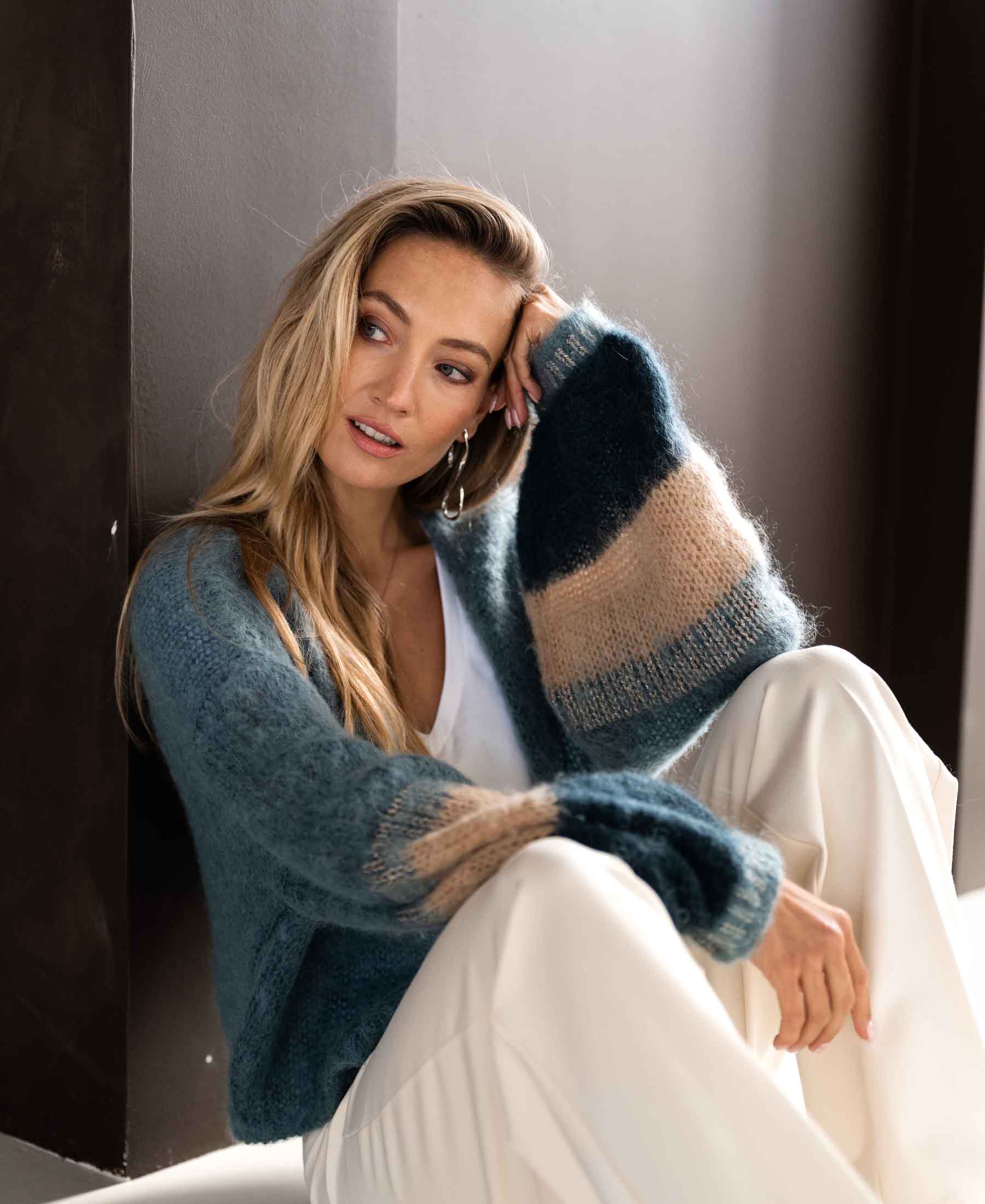 Mist green fluffy vest made of soft material, shown on a model sitting on the floor, side view.
