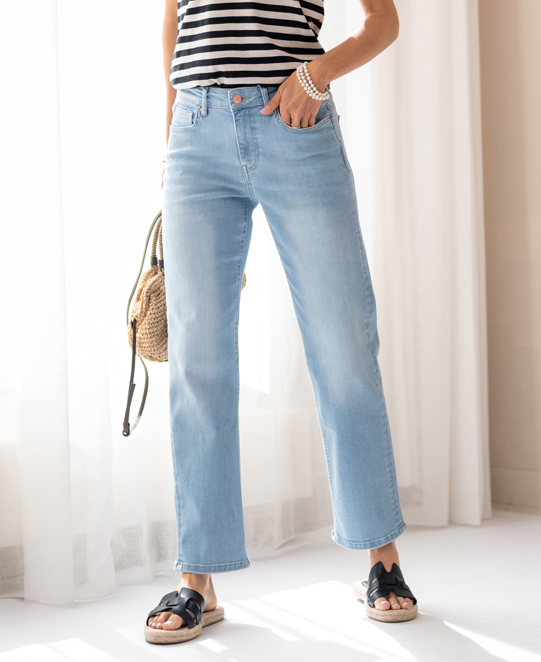 A person wears light-wash cropped jeans by Plein Publique, standing by a window.