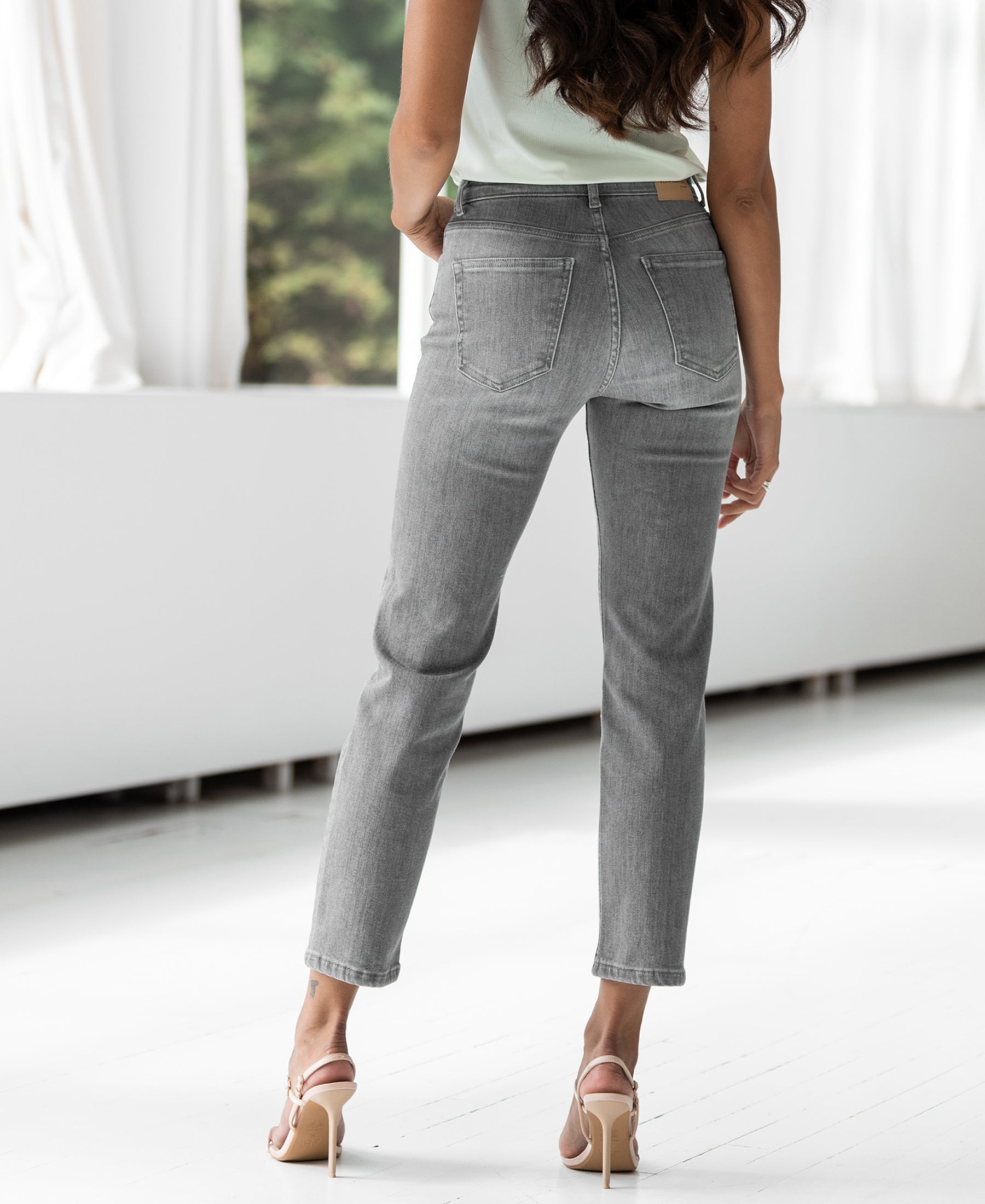 Back view of grey stonewash cropped jeans, shown indoors.
