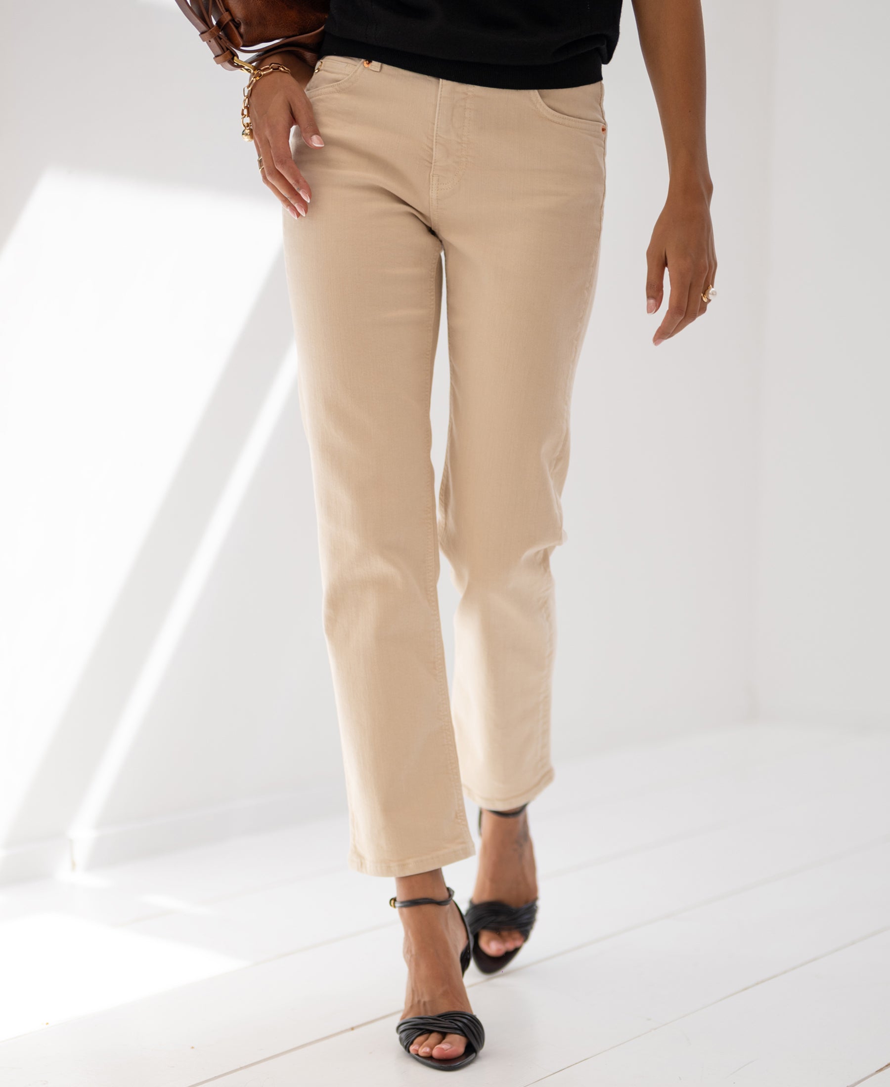 Person wearing cropped sand-colored jeans by PLEIN PUBLIQUE stands in a bright, minimalist room.