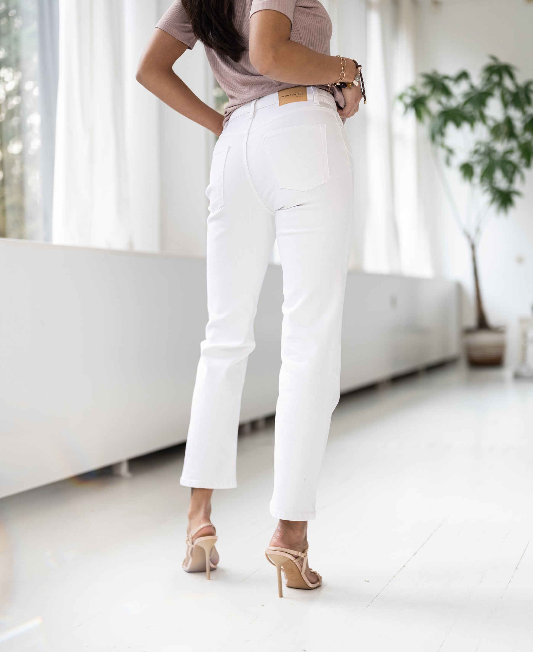 Woman indoors wearing white cropped jeans in a bright modern room.