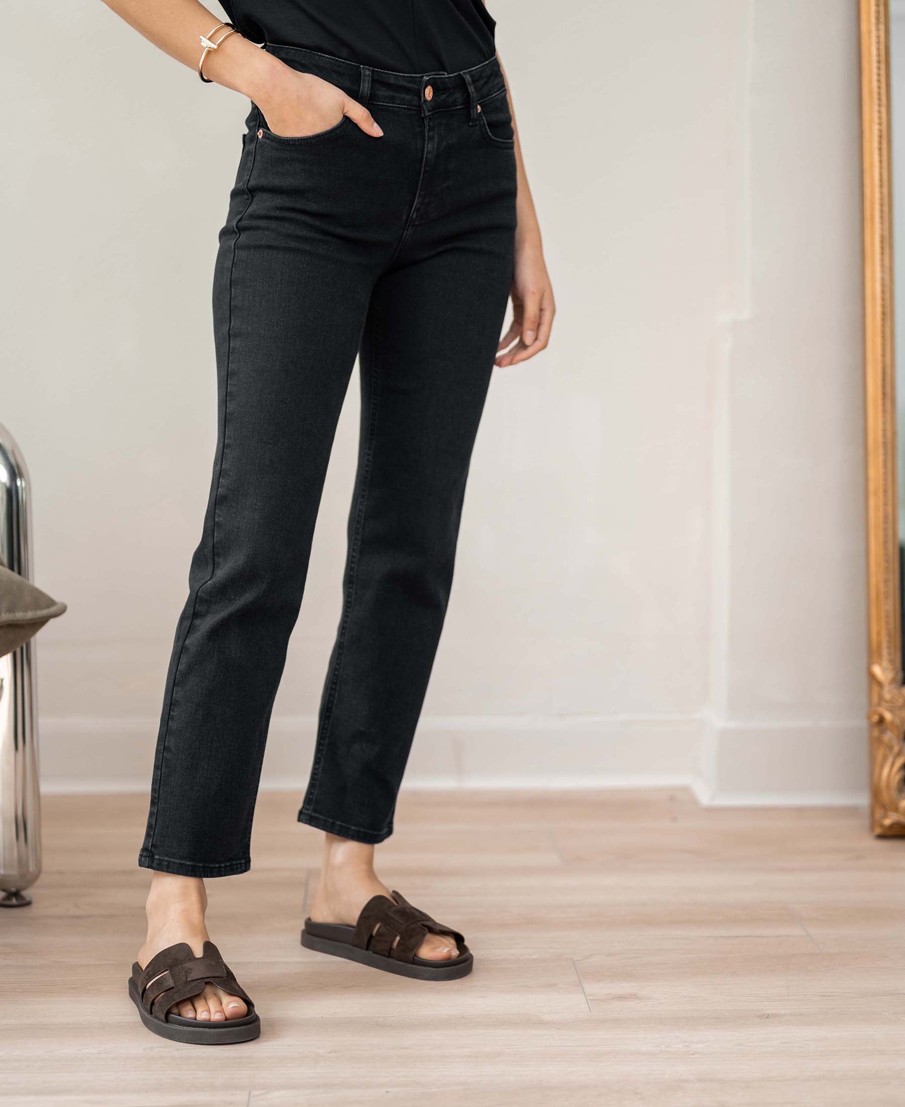 Person wearing black 7/8 cropped jeans with one hand in pocket.