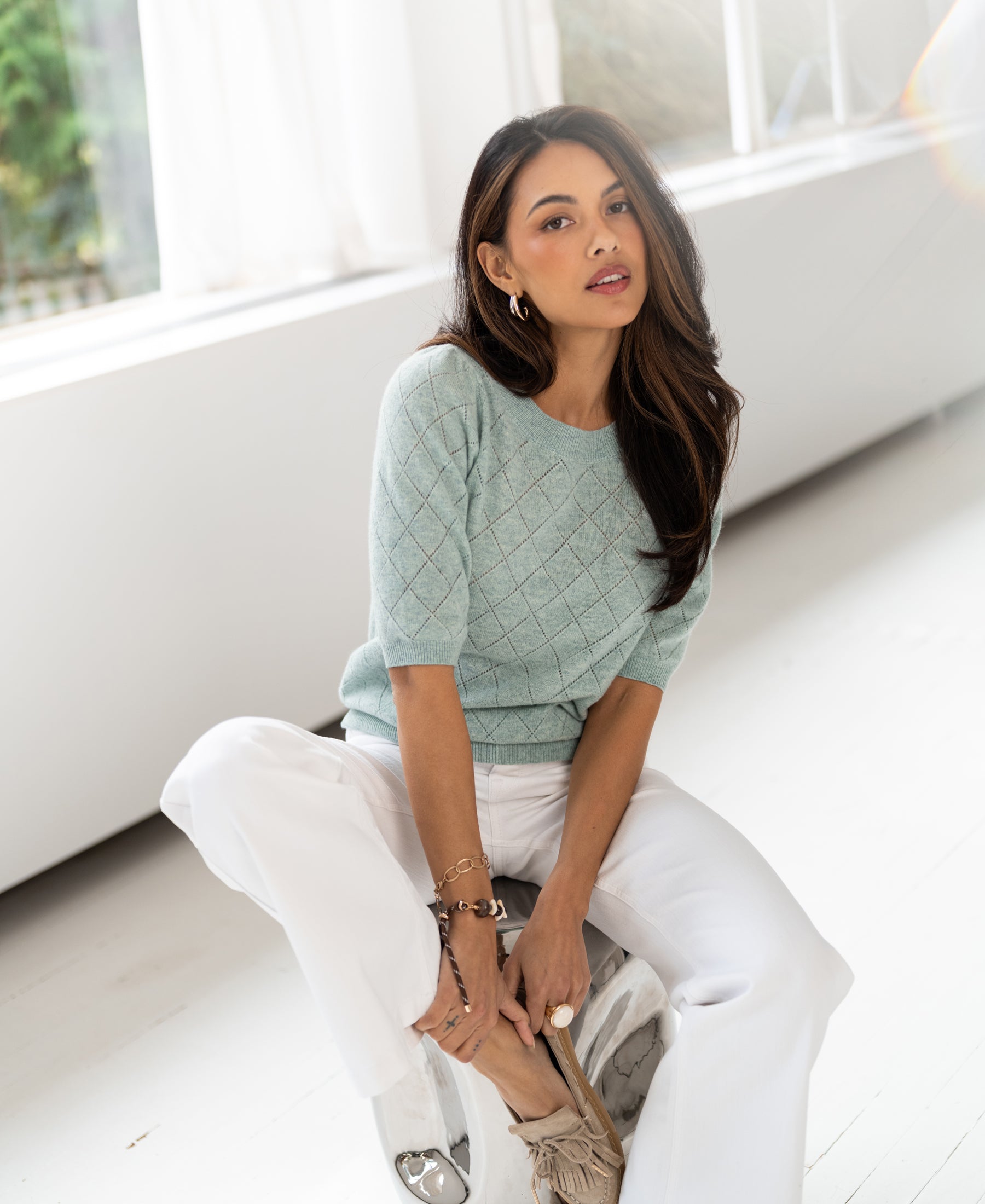 Mist green argyle merino sweater, shown worn by a woman seated indoors facing the camera.